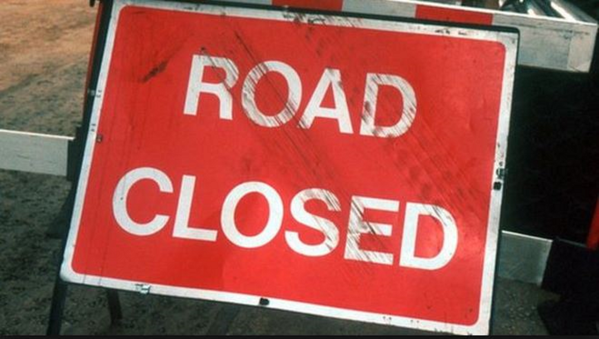 A battered red sign with road closed in white lettering