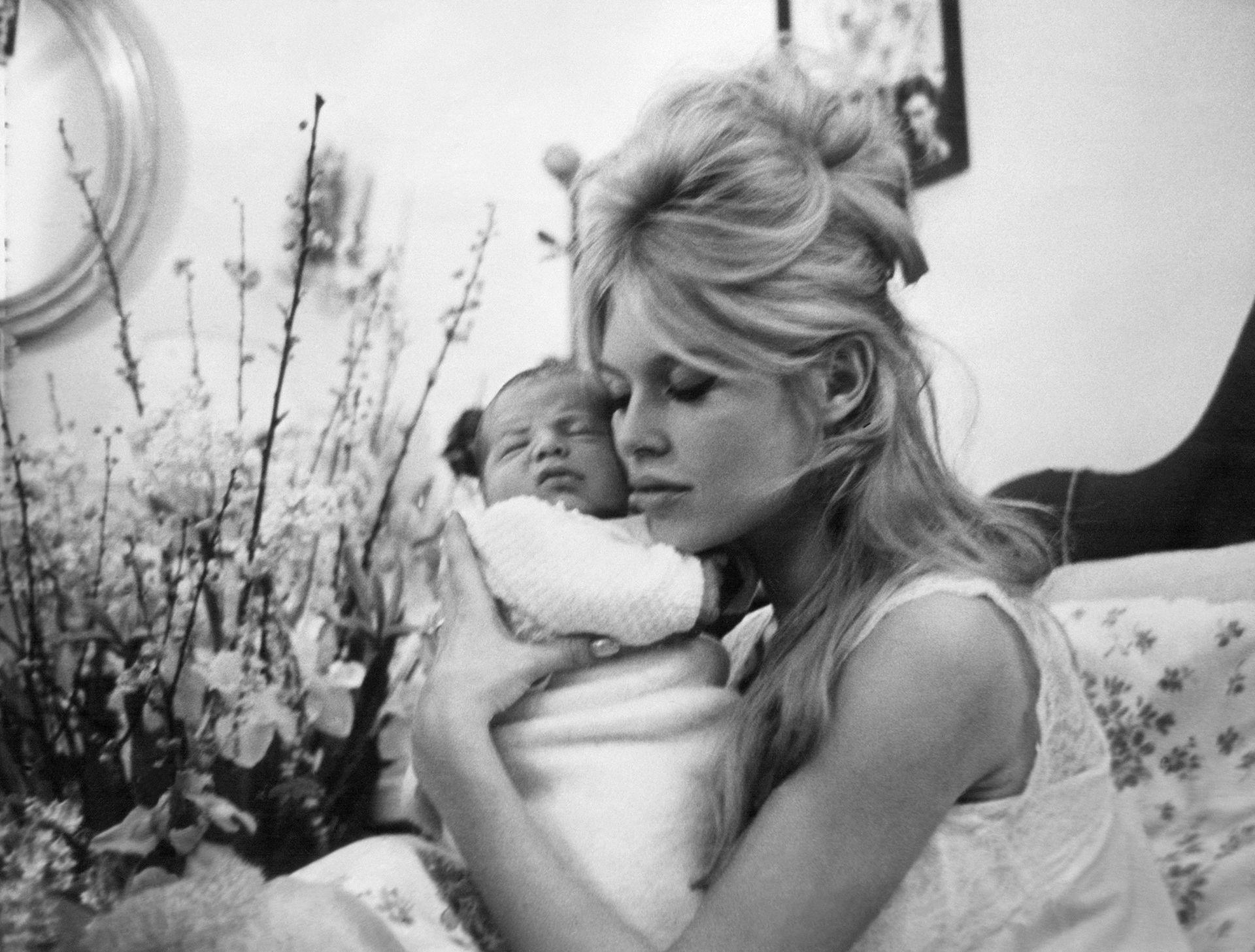 Brigitte Bardot, e veshur me një këmishë nate me flokët e saj bjonde të modeluara në formë koshereje bletësh, duke e mbajtur të birin afër fytyrës.