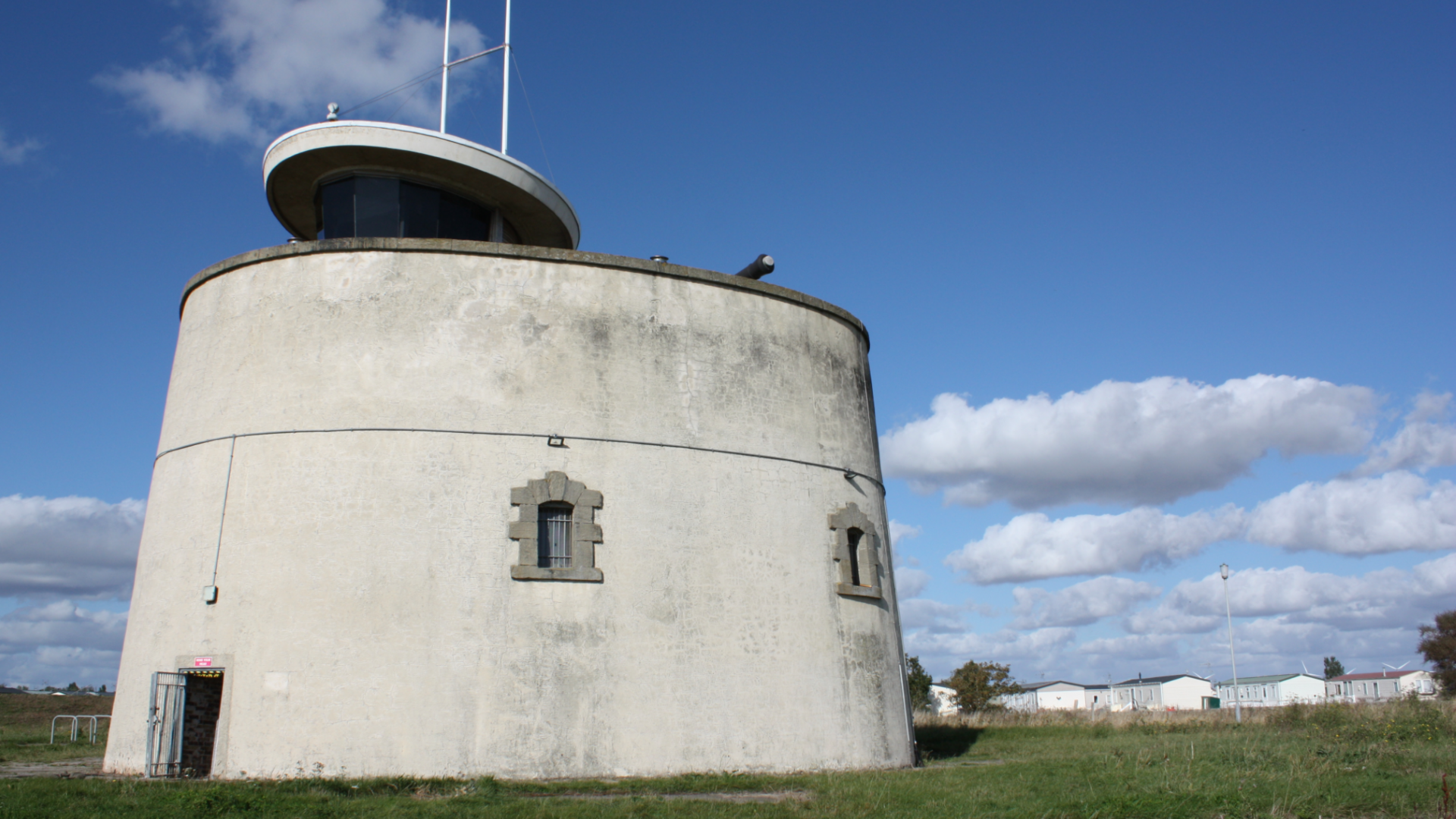 Jaywick Martello Tower, which is a circular fort made of white stone. It is set in a field and has been pictured on a bright day.