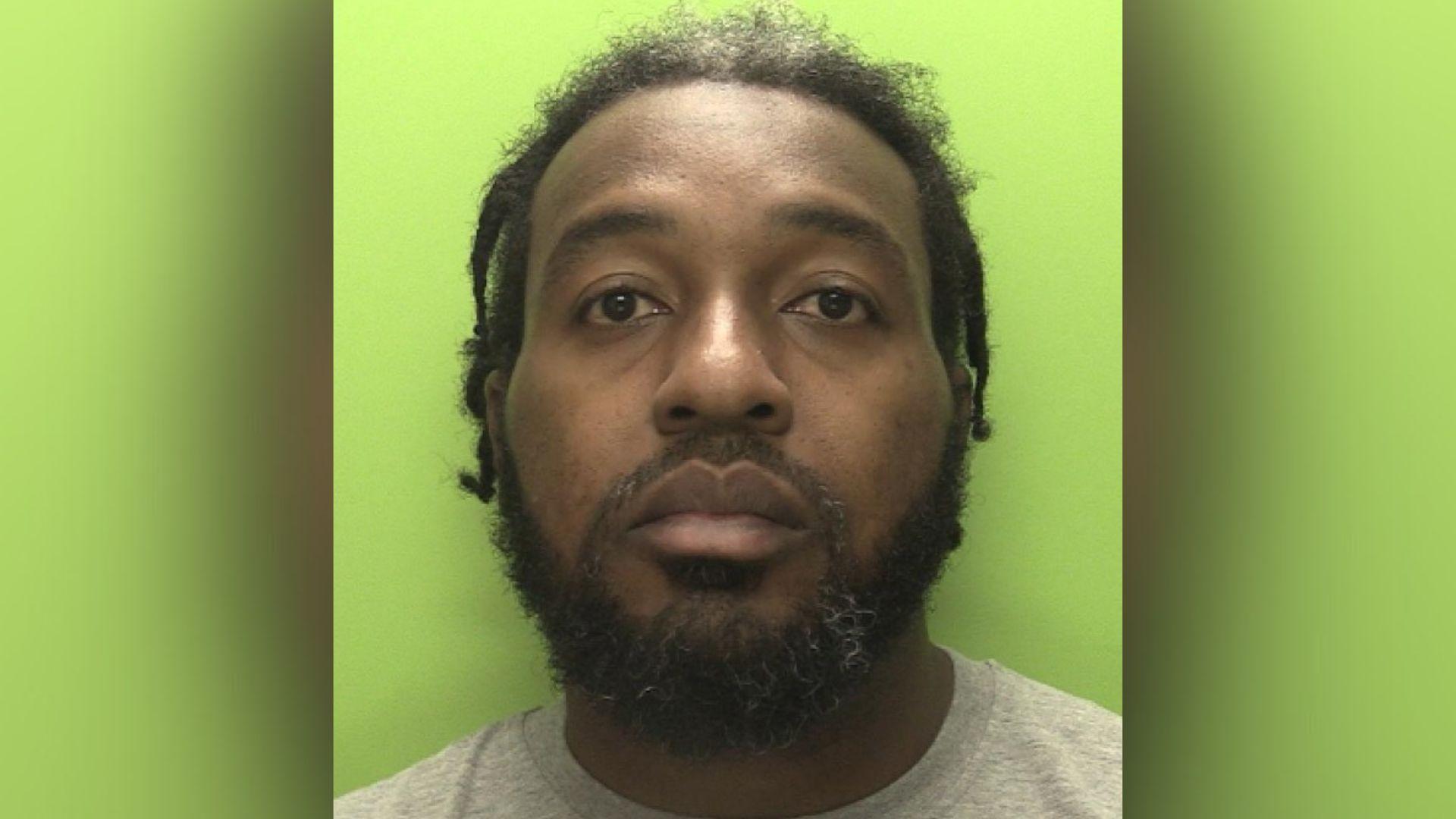 A police image showing a man with dreadlocks standing in front of a green background.