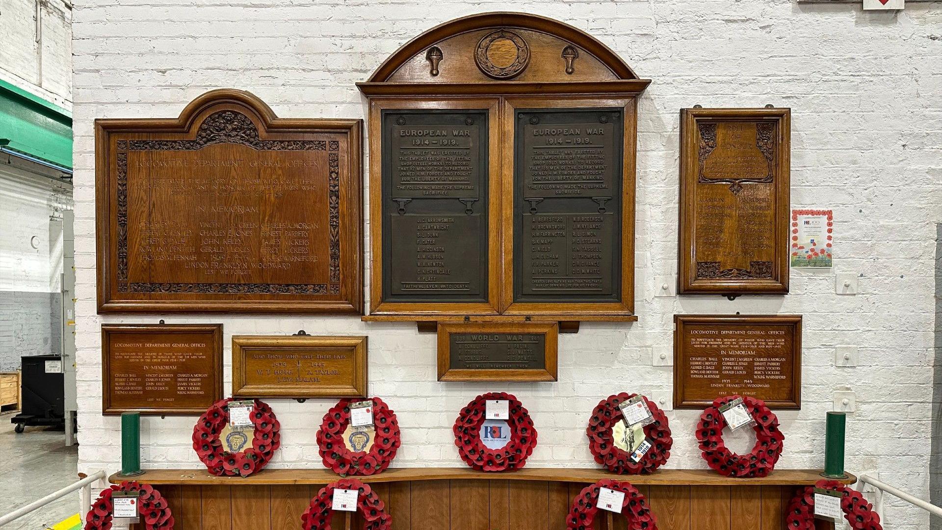 The war memorial plaques at Crewe Works. They contain poppies and engraved names of fallen soldiers and have names inscribed on wooden tablets.