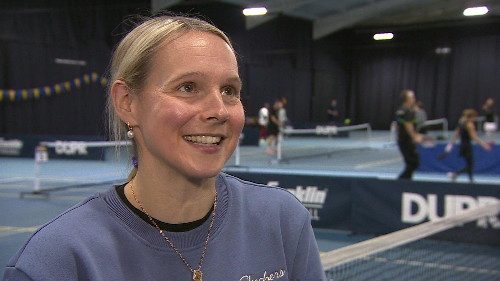 England Pickleball player Thaddea Lock smiling while being interviewed. There are players behind her on the court.