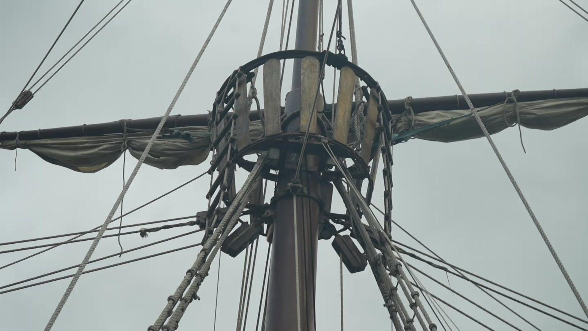 A close up of the ship's viewpoint toward the top of ones of its masts. Rope ladders lead up to the viewpoint and sails are tied up behind it. 
