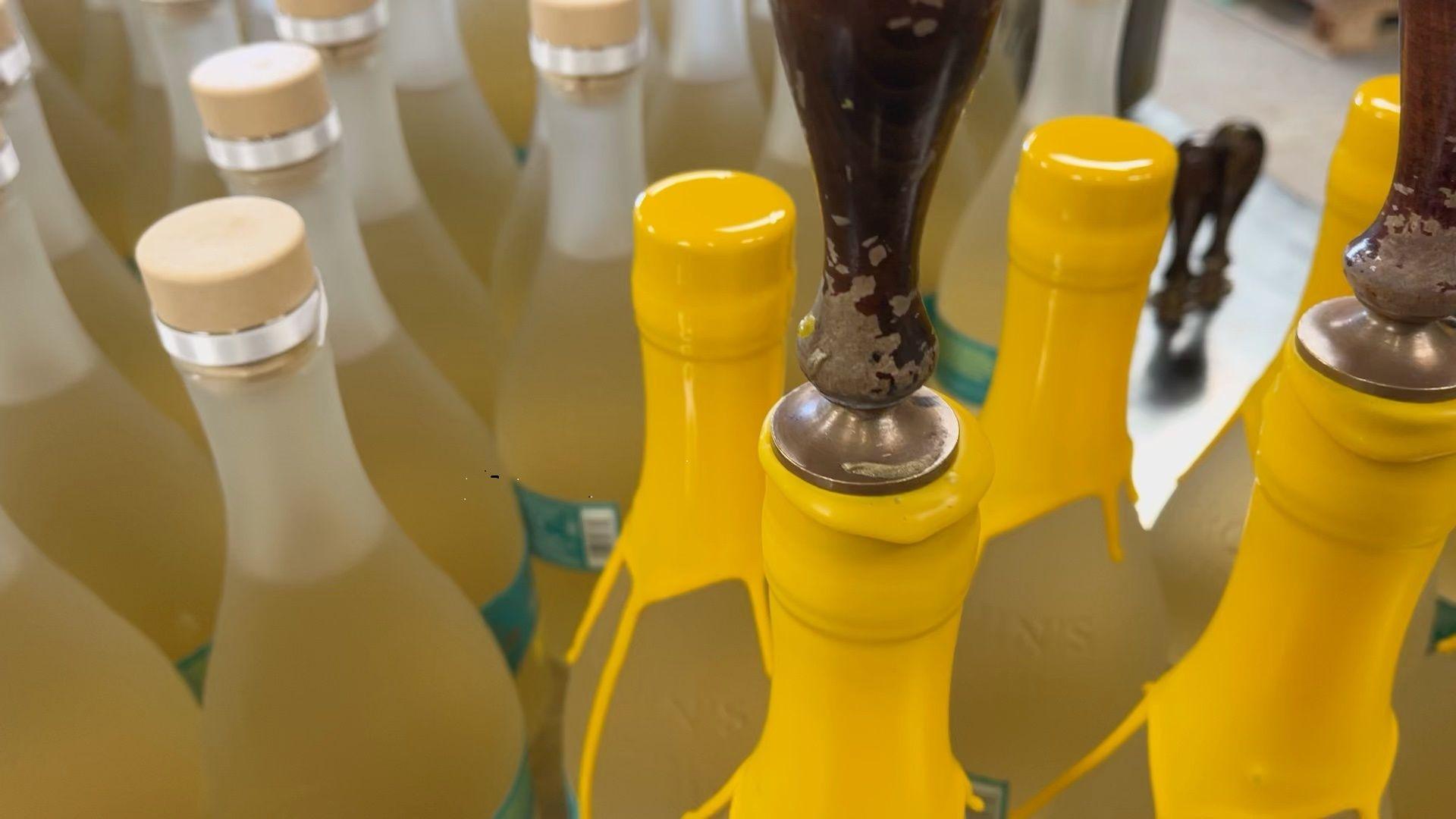 Stamps are put onto hot wax used to seal bottles at the Tarquin's bottling facility. The hot yellow wax can be seen dripping down the neck of the bottles.