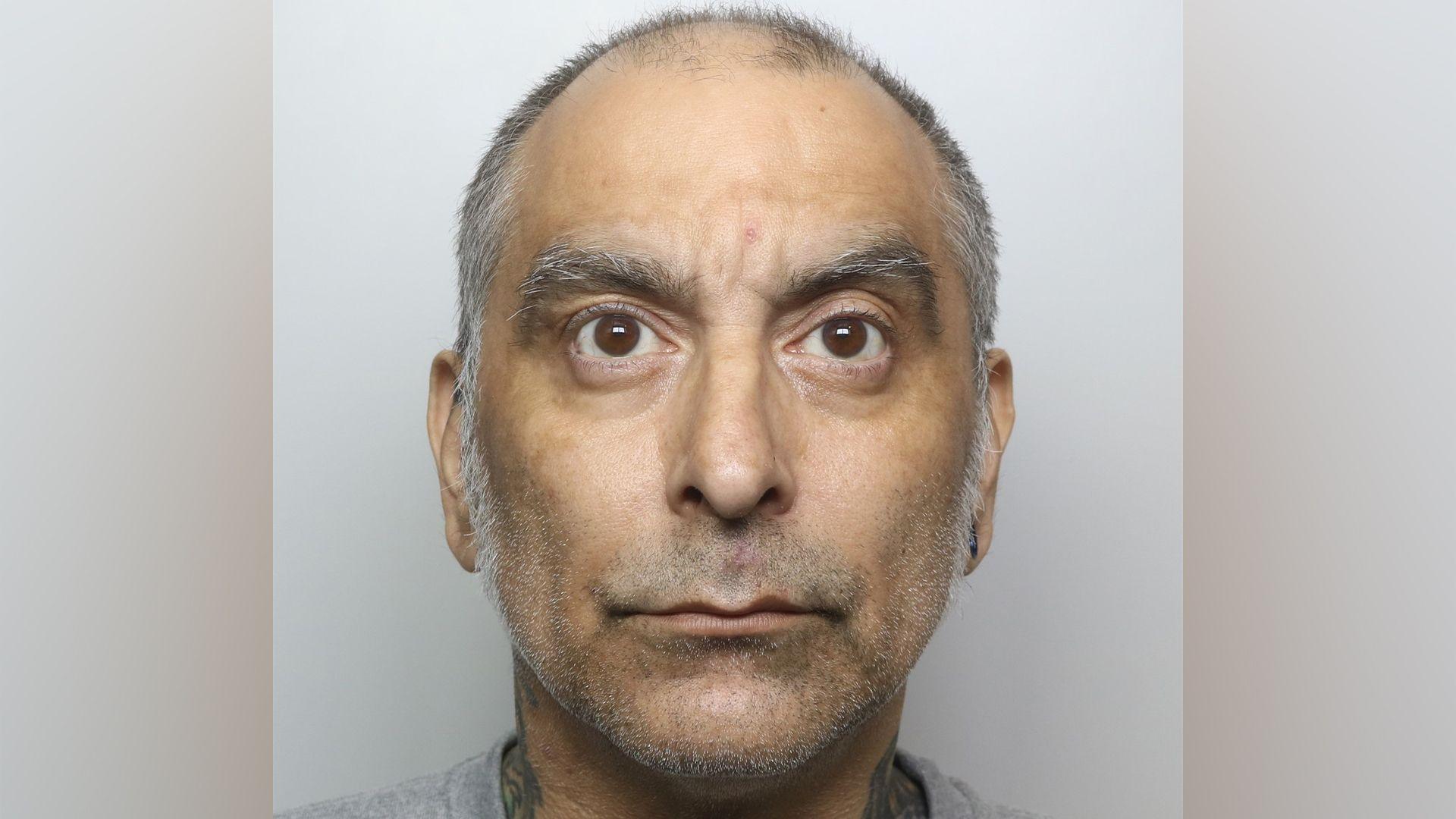 A mugshot photo featuring a man with large brown eyes and grey eyebrows, with short grey receding hair.