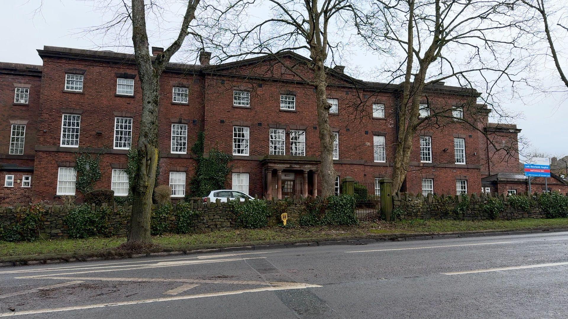 A red brick building with a sign to the far right that signposts Leek Moorlands Hospital - Minor Injuries and Illnesses Unit.