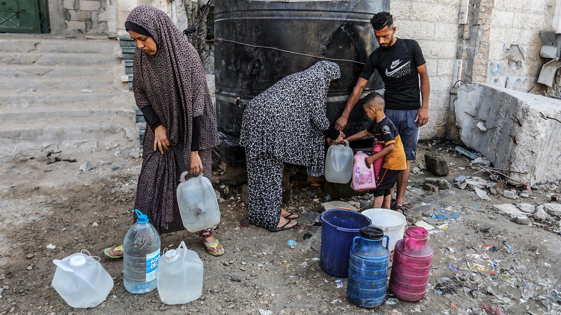 A group of Gazans including a man, two women and a child fill gallon bottles with water from a black water tank on the side of a street in Khan Younis in Gaza on 21 May.