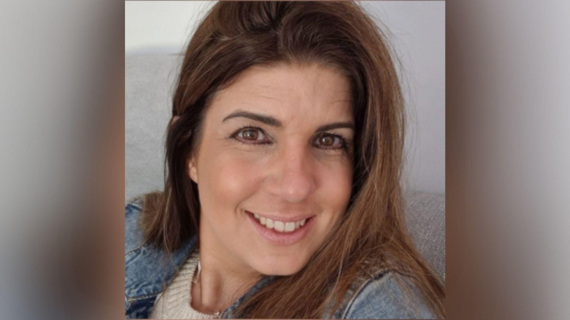 Suzie Cronin with long dark brown hair smiling at the camera and wearing a denim jacket with a white top underneath.