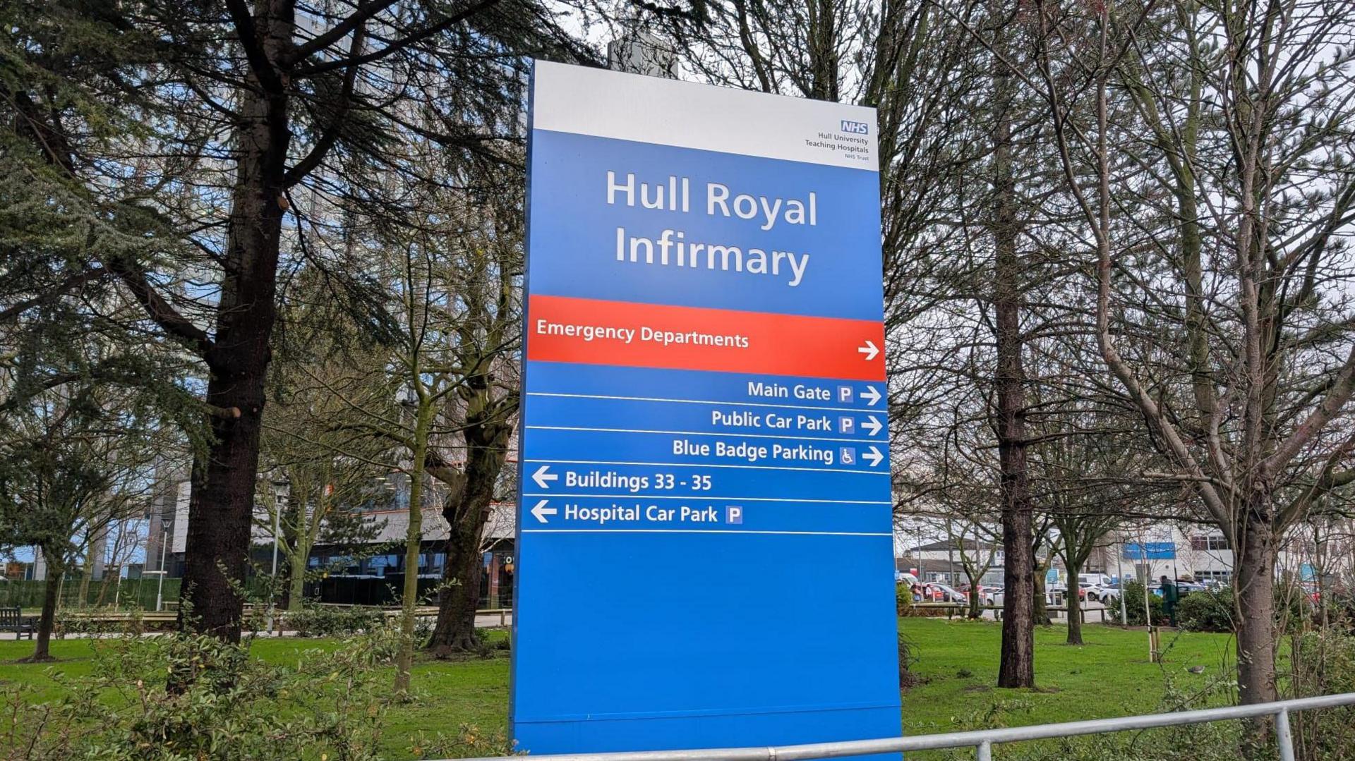 An image of Hull Royal Infirmary's main sign, with the hospital itself in the background behind a landscaped garden area.