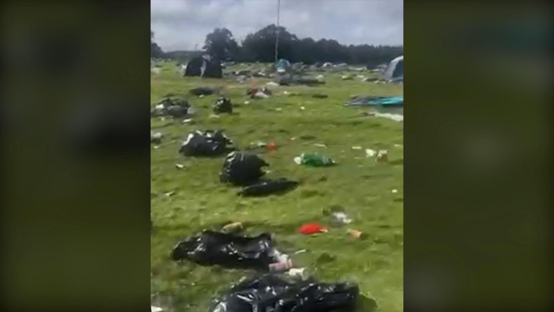 A still image from a video showing black bags and rubbish strewn around a green field