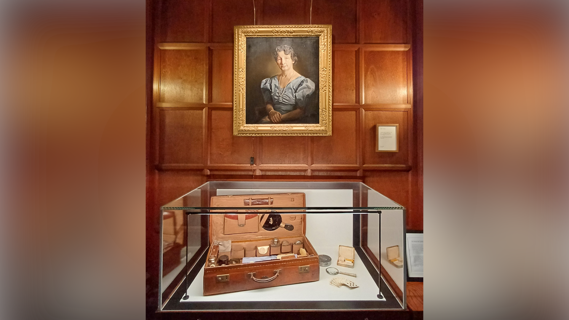A brown leather suitcase sits in a glass box in front of a portrait of Mrs Edith Pretty.