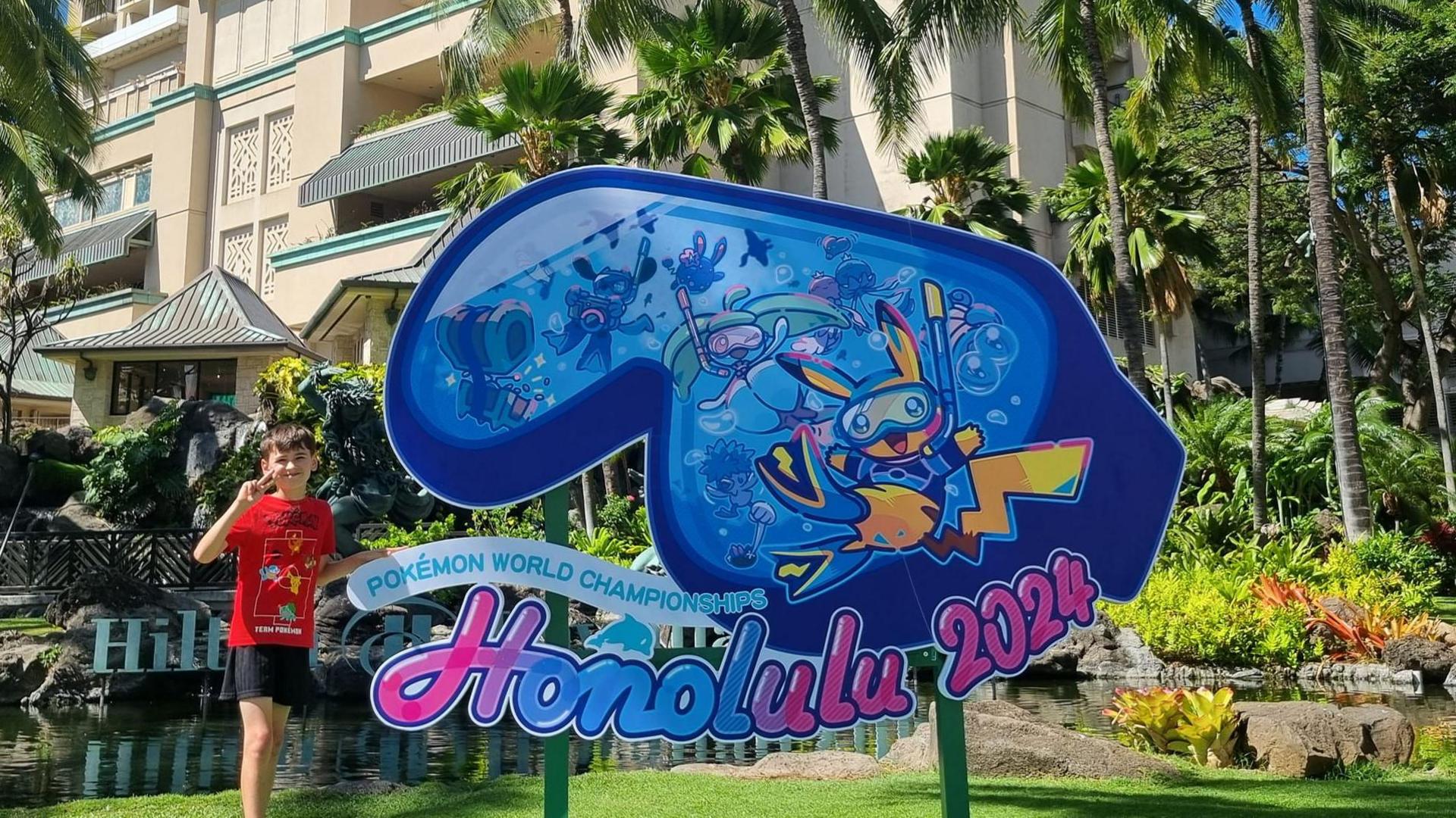 9 year old Declan stands next to Honolulu 2024 Pokémon World Championship sign 