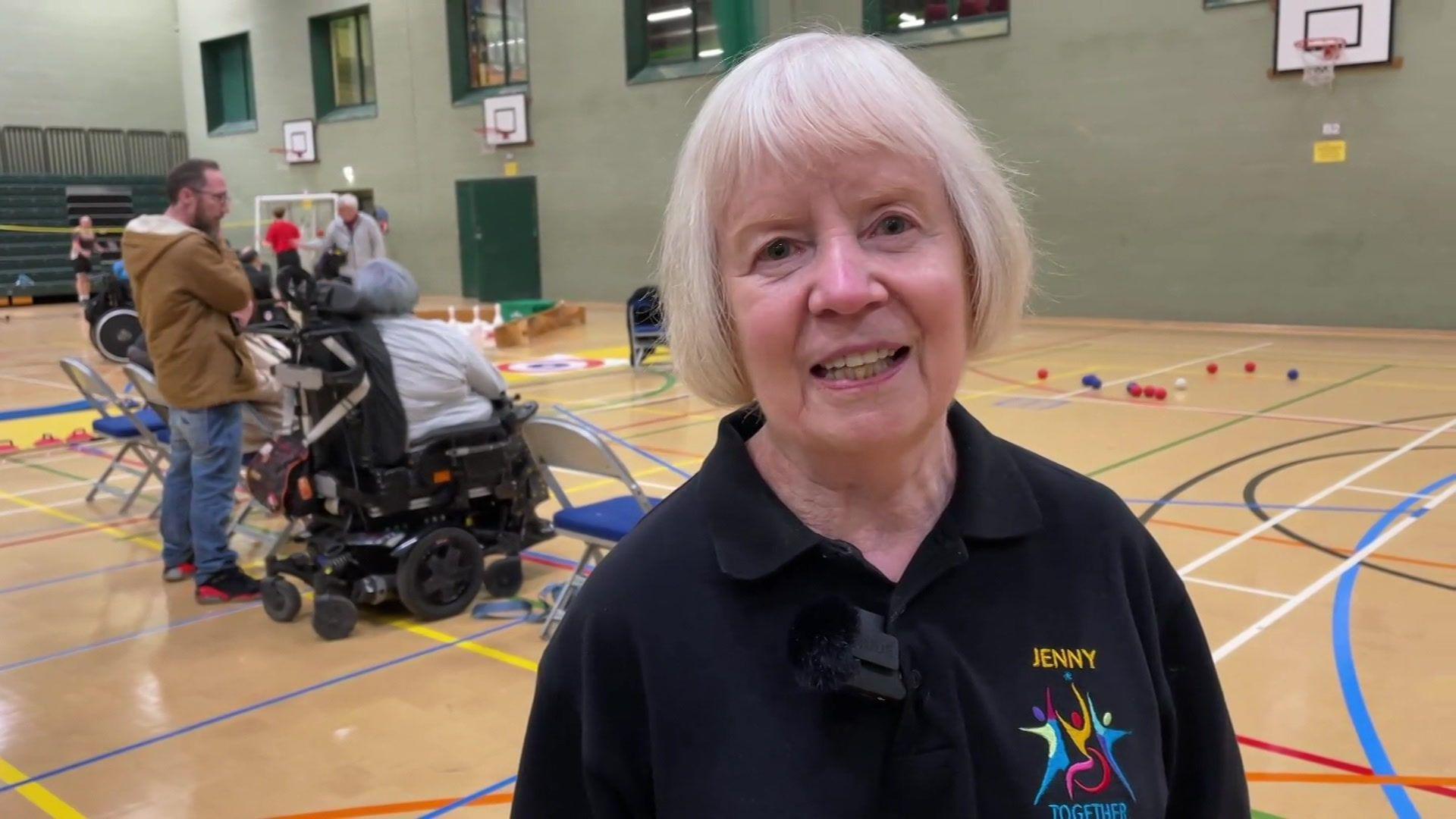 Jenny Morris is wearing a black polo shirt with short grey hair inside a sports hall.