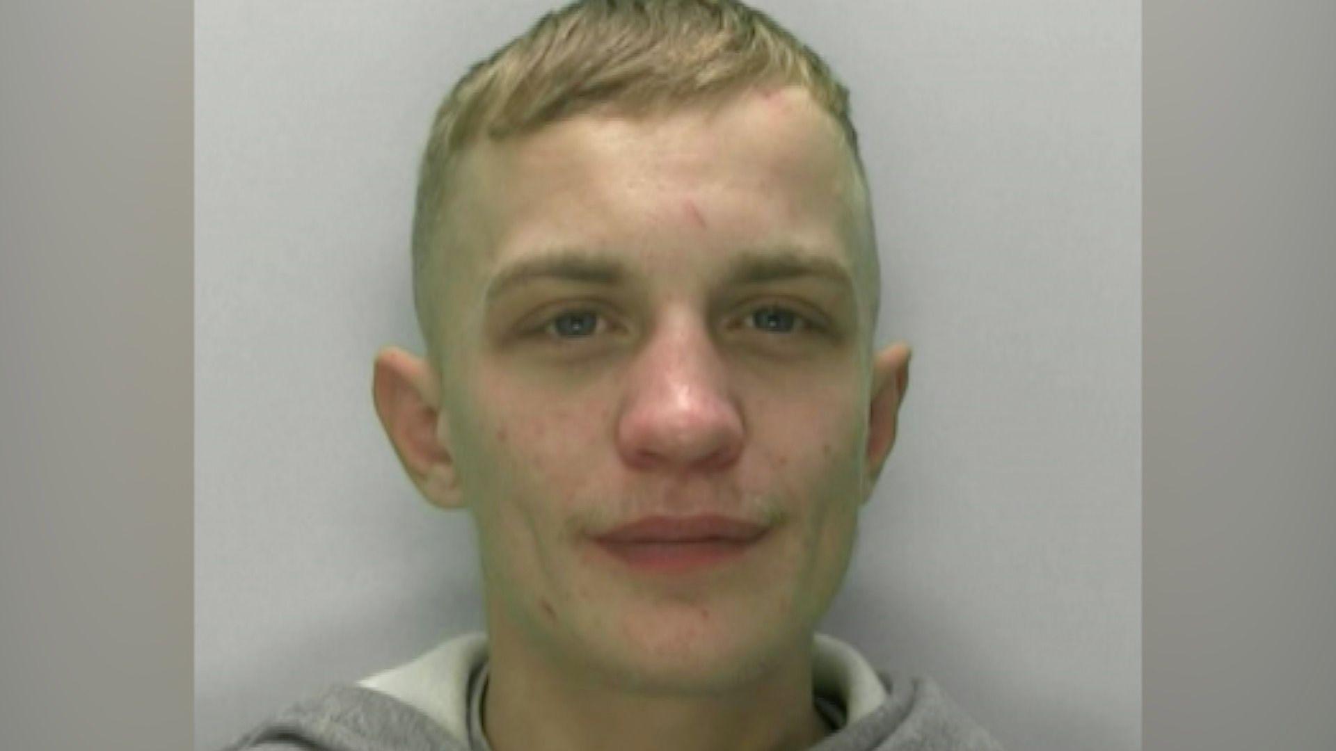 Jack Bradley appears to be smiling slightly in his police mugshot as he stares just off-camera. He is standing against a grey-white background, wearing a grey hoodie with a white inside. He has short blond hair.