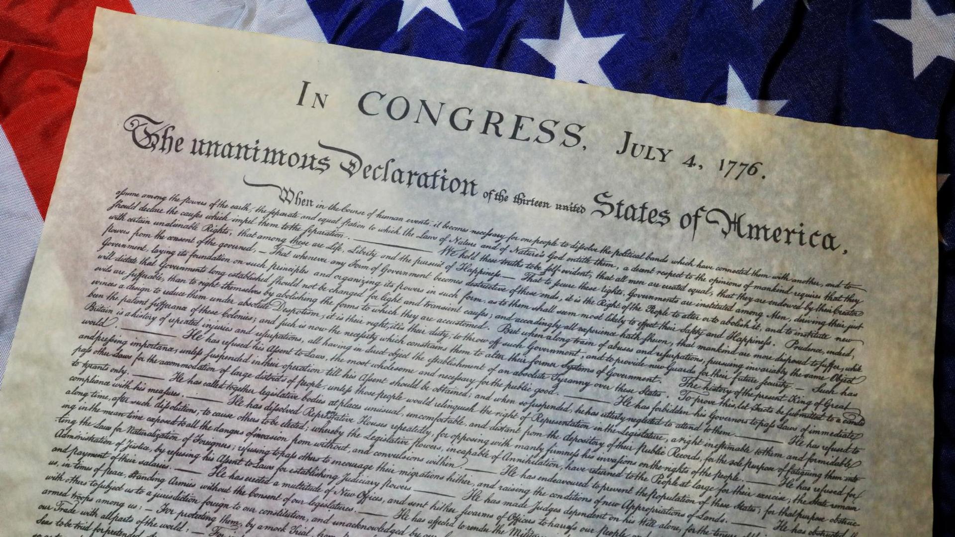 A copy of the Declaration of Independence sitting on top of the flag of the USA.