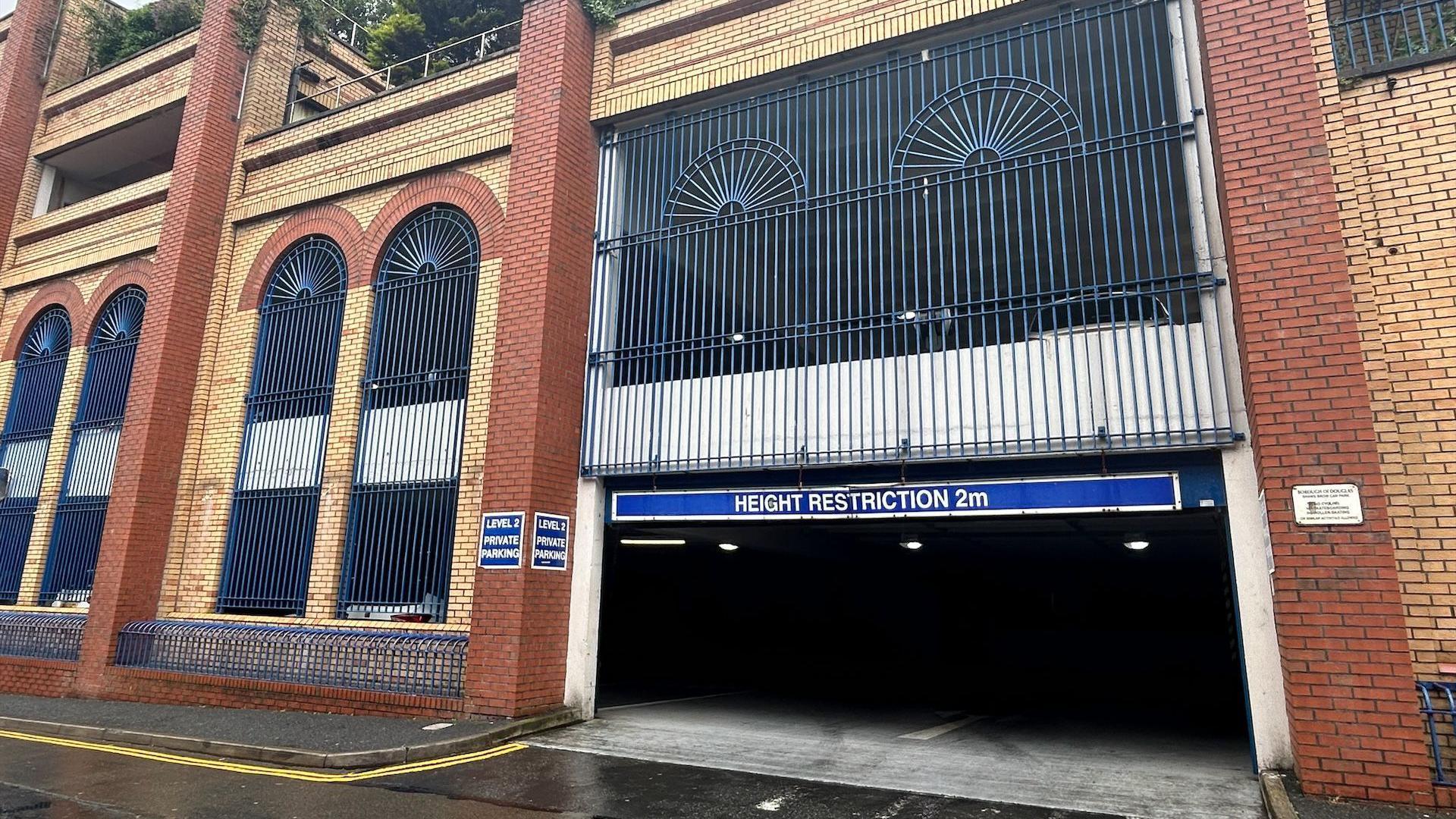 The red and yellow brick Shaw's Brow building with arched window shapes and blue vertical metal bars.