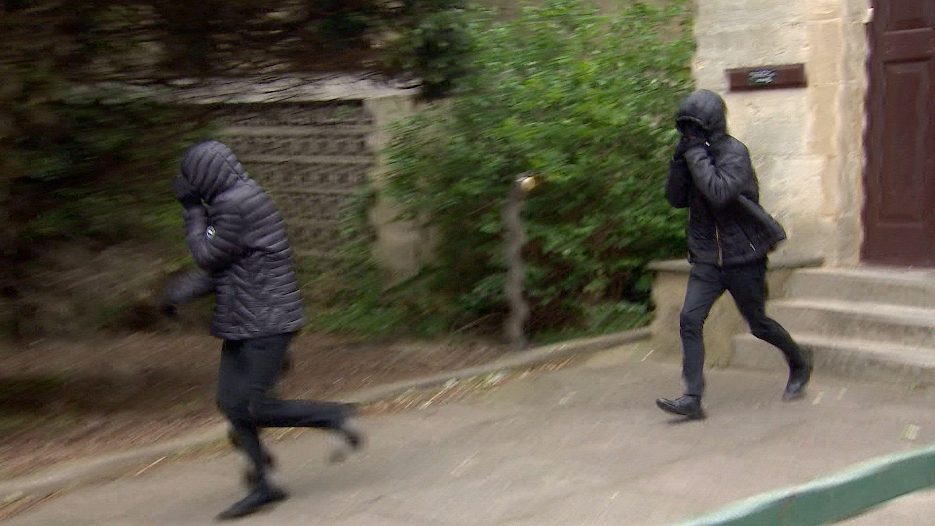 Two people in black covering their faces his hoods and their hands