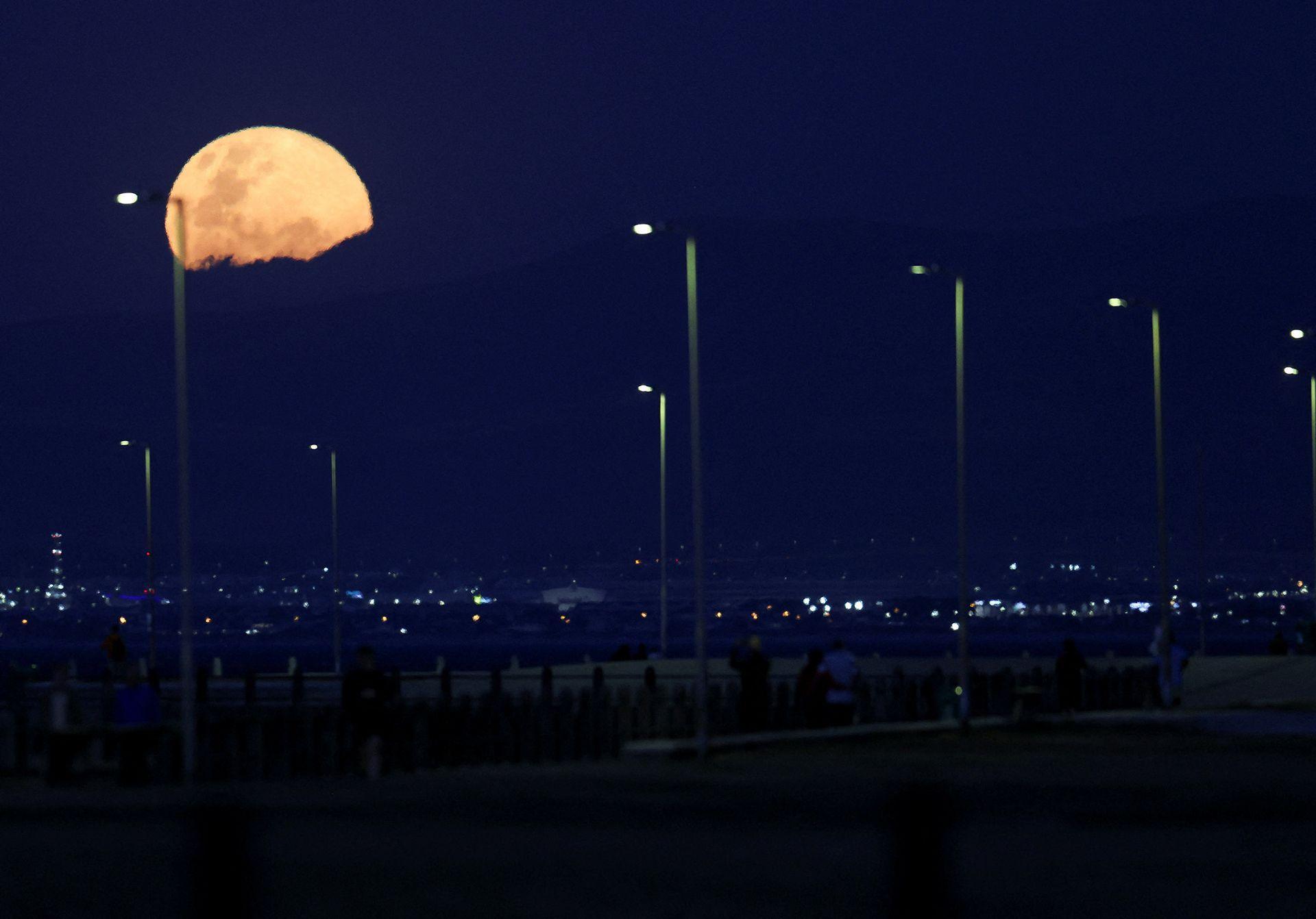 An orange moon hangs over street lights against a very dark sky in Cape Town on Wednesday