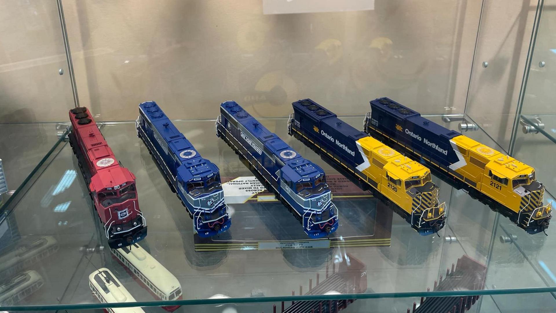 A display case with five model trains in various colours