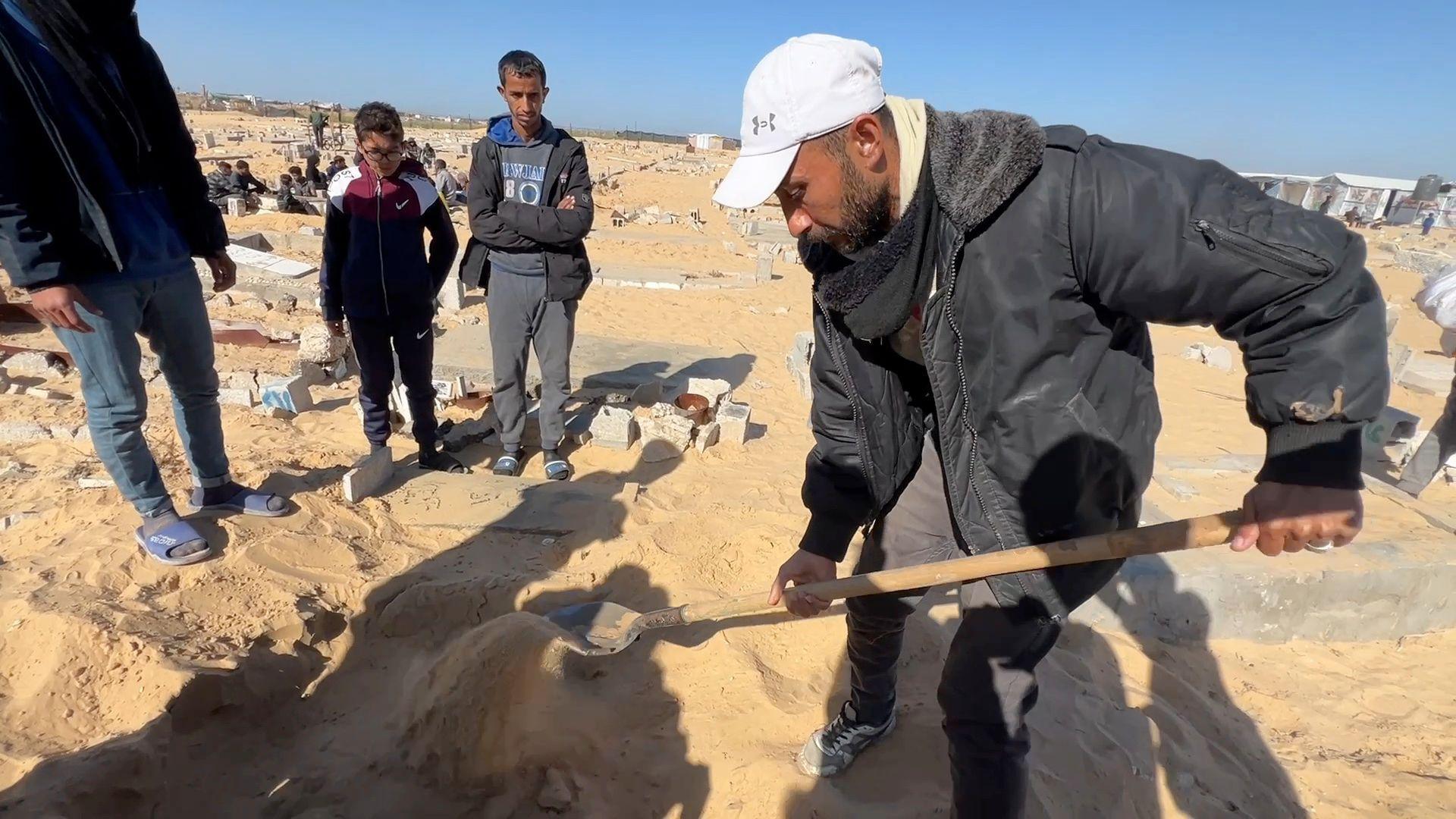 A man is seen with a shovel at a gravesite in sand