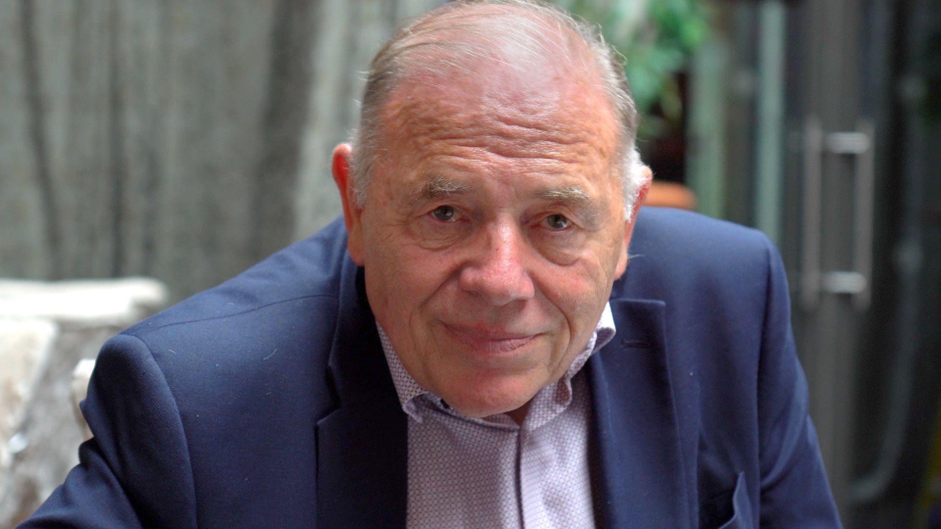 Martyn Sayers, wearing a blue suit and light purple shirt, sitting in his nightclub.