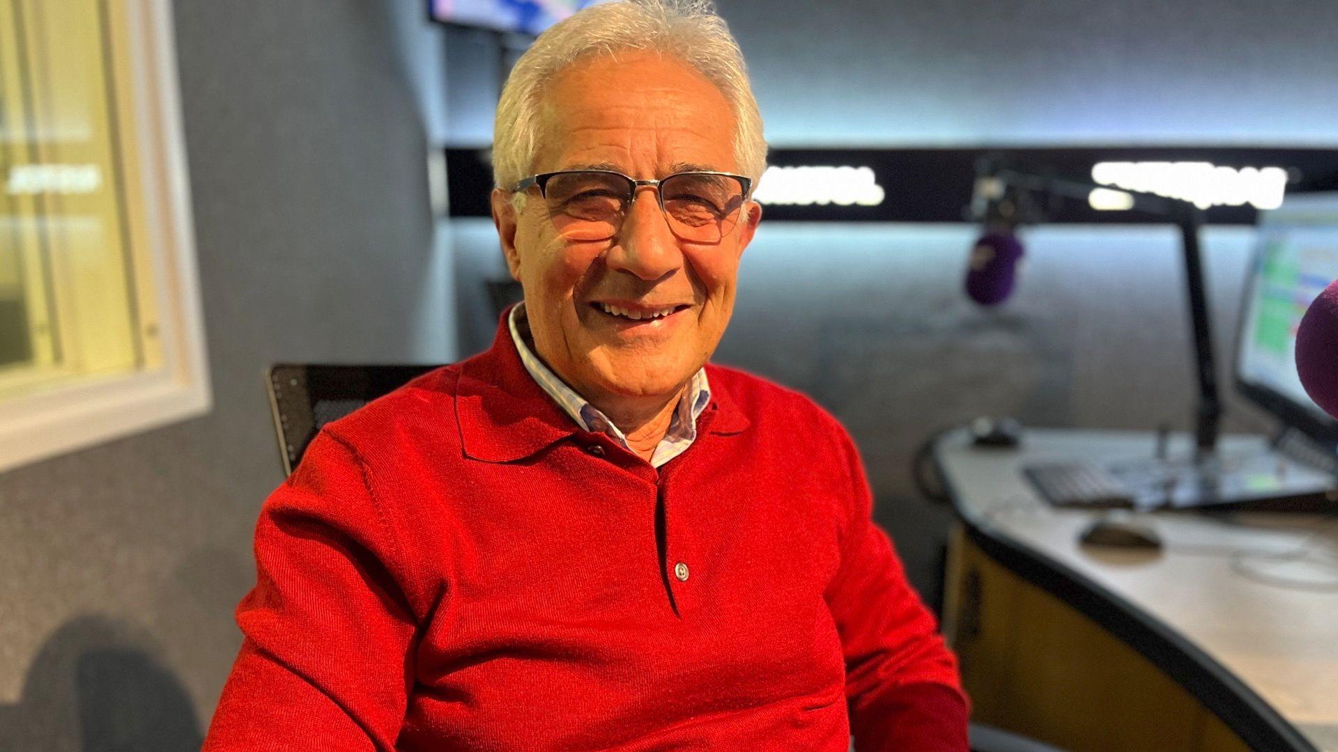 Gianni wearing red polo shirt with short, grey hair and glasses smiling at the camera