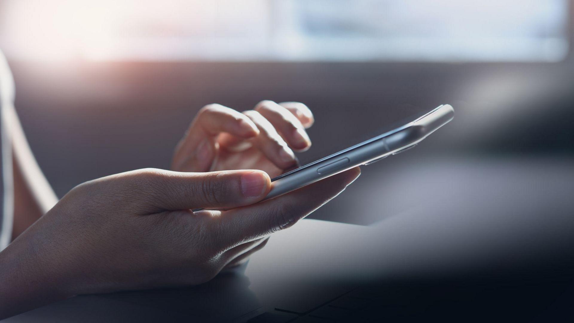 Close up photo of a person's hand holding a mobile phone with a blurred background.