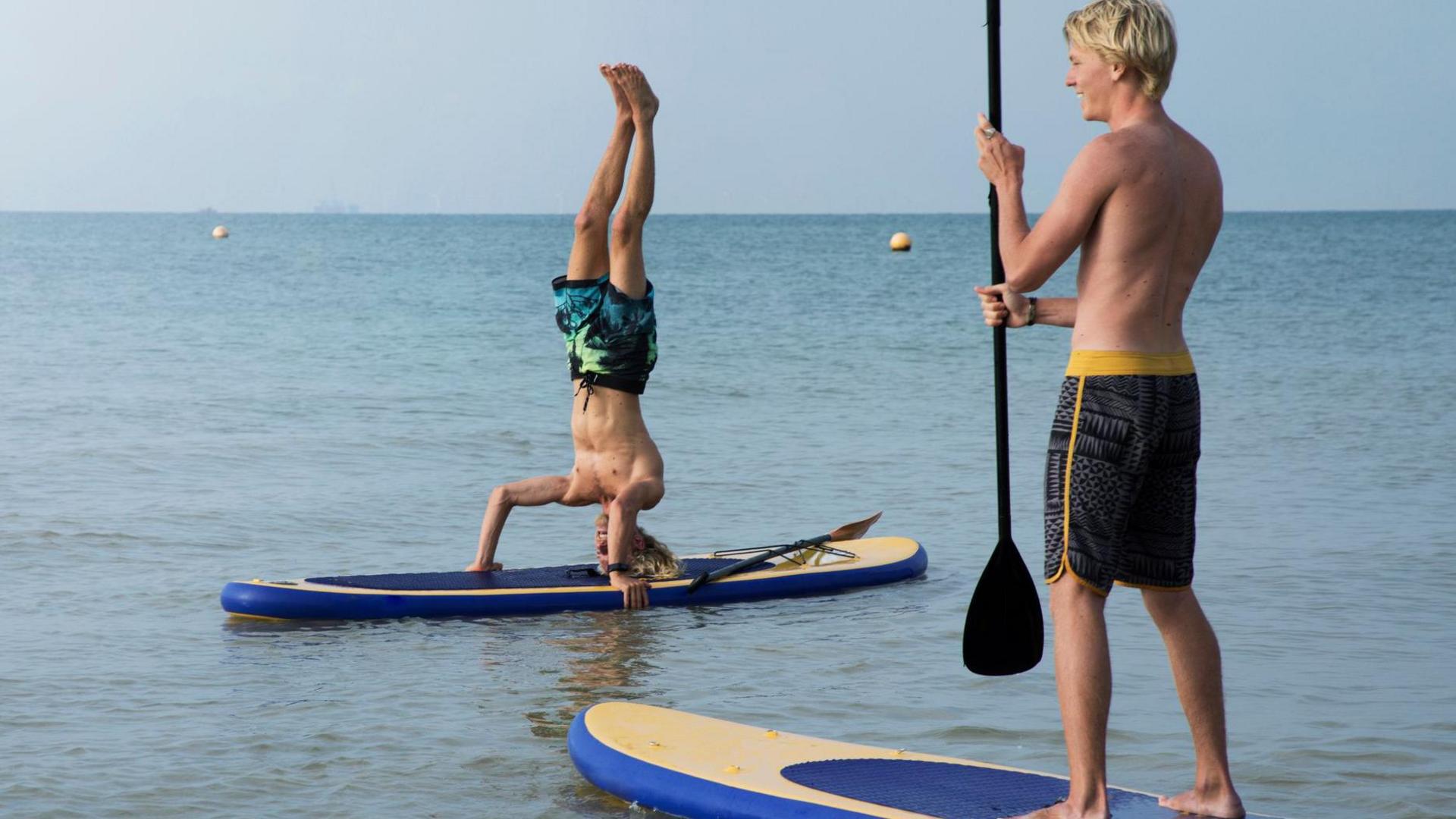 Two men on paddleboards, and one is doing a handstand