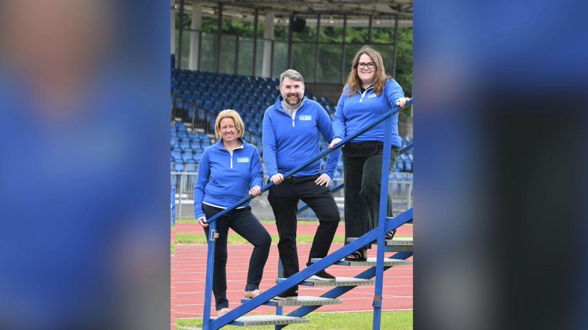 A man between two women smiling on blue steps with matching blue jumpers