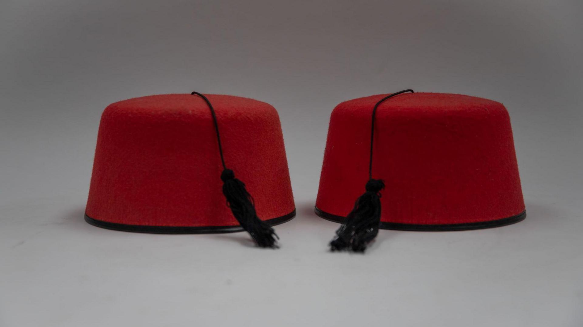 Two red fezzes, rimless hats with black tassels, photographed on a plain white background.