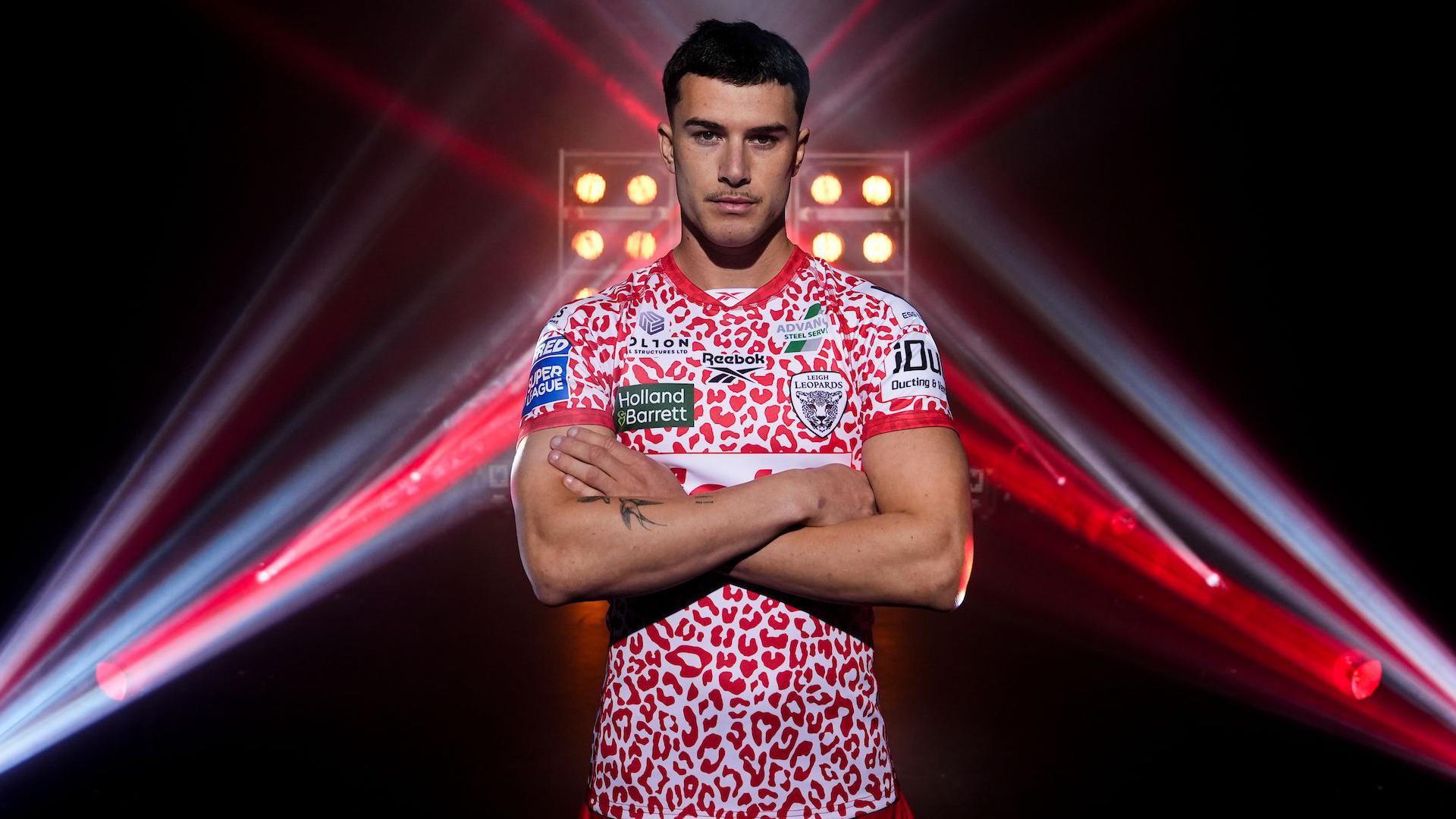 David Armstrong stands arms folded in front of a series of upward facing light beams in his leopard print Leigh home shirt