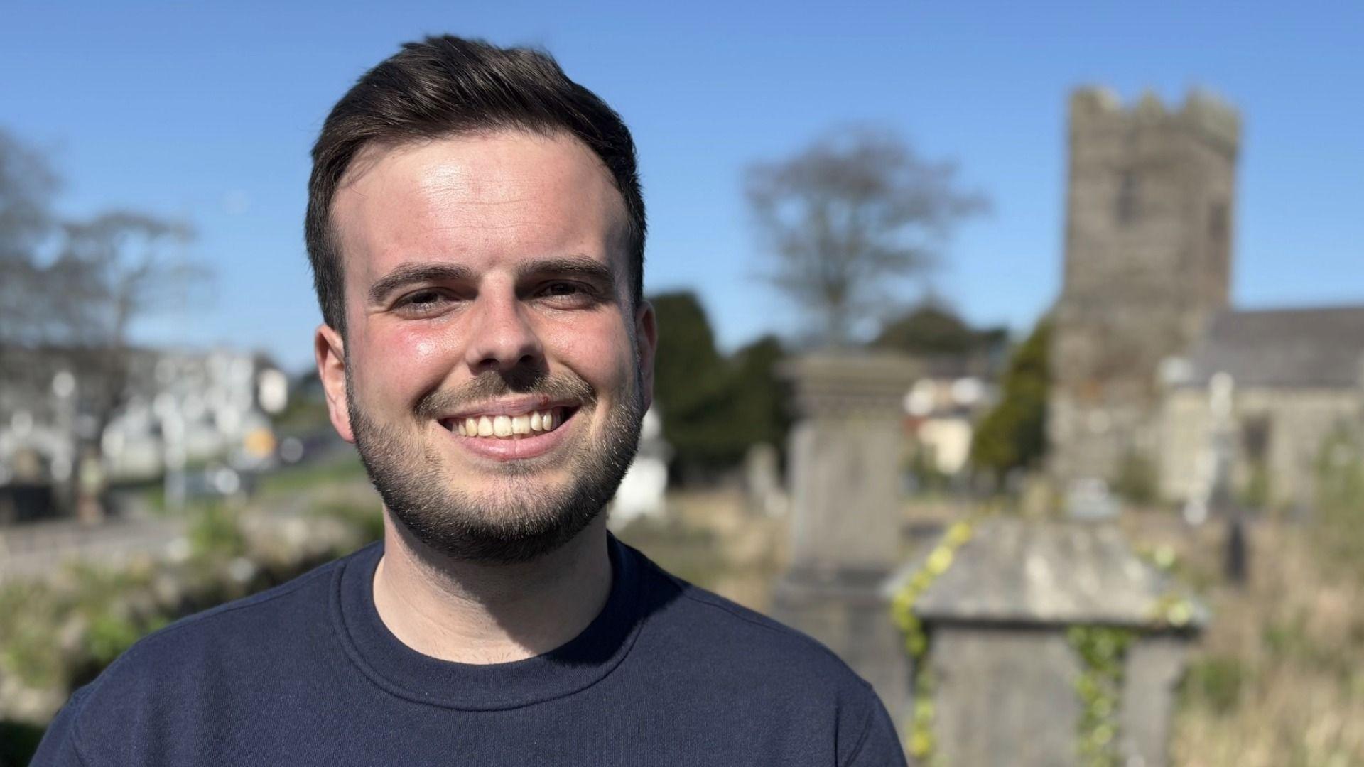 Y Cynghorydd Dewi Jones ger Eglwys Llanbeblig, Caernarfon