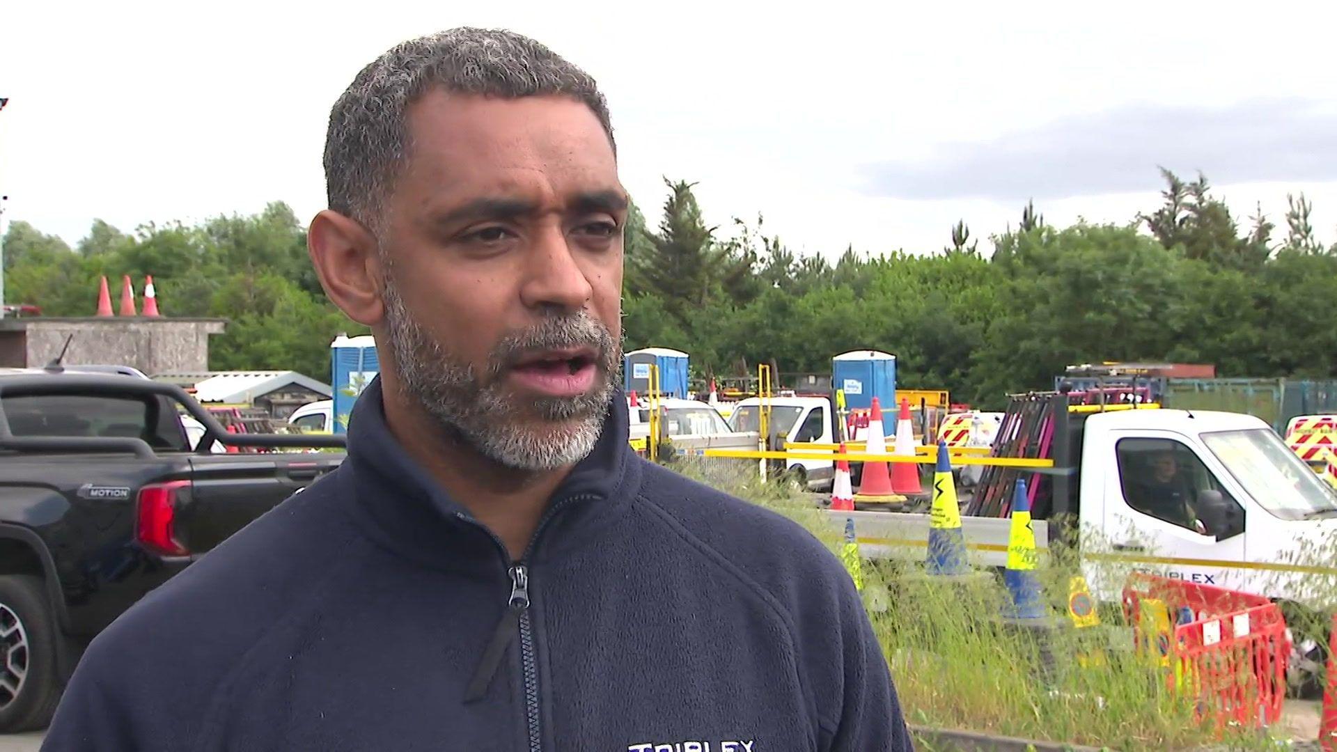 A man in a blue fleece jacket is standing in front of some cars. 