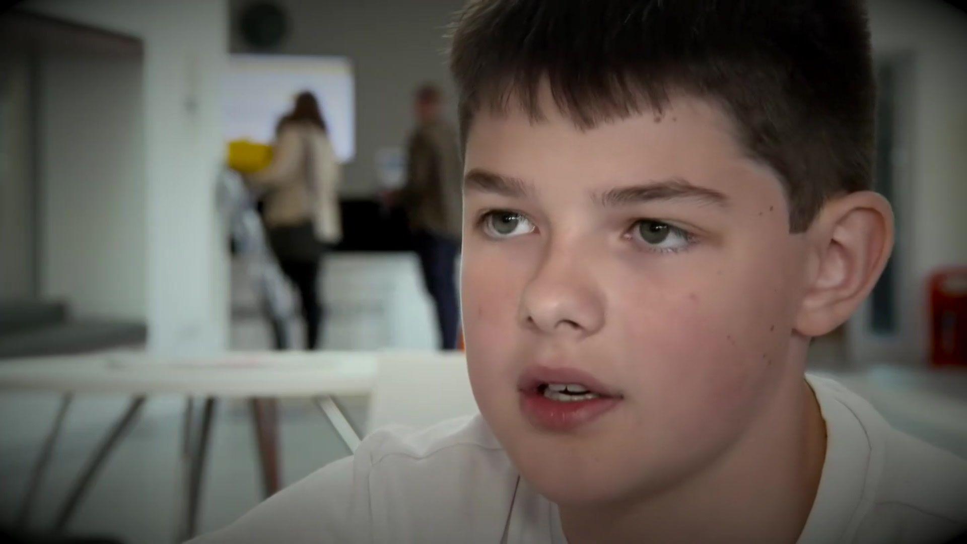 Aaron, wearing a white t-shirt, speaks to the camera in 2019