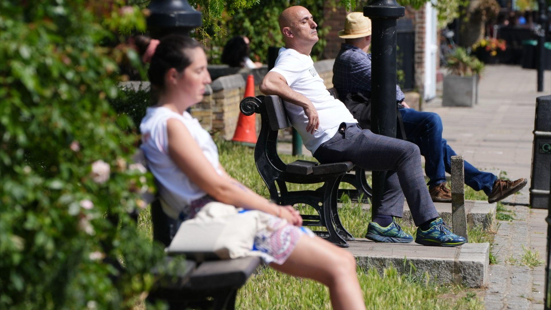 People sit on park benches to soak up the sun in the UK. 