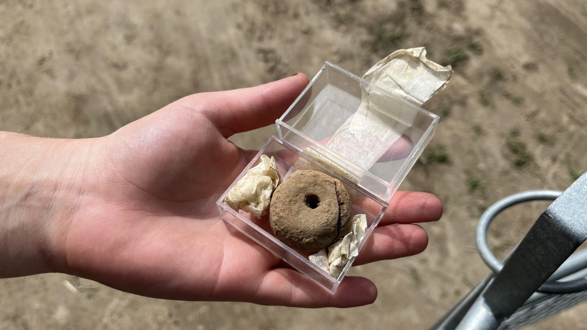 Spindle whorl - a flattened cylinder with a hole through the middle - in a clear box held in a hand