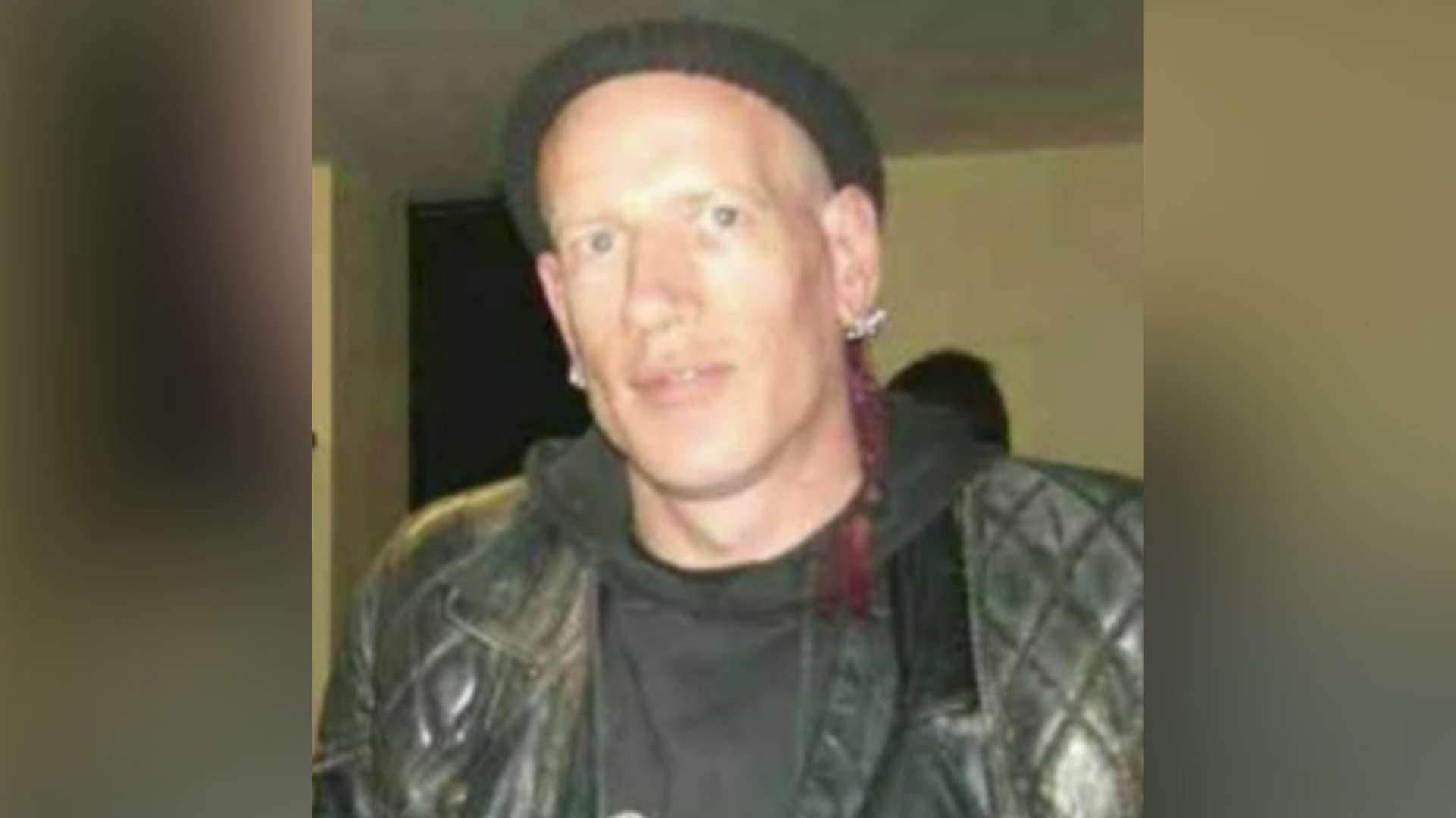 A man, wearing a black hoodie, black leather jacket and black hat.