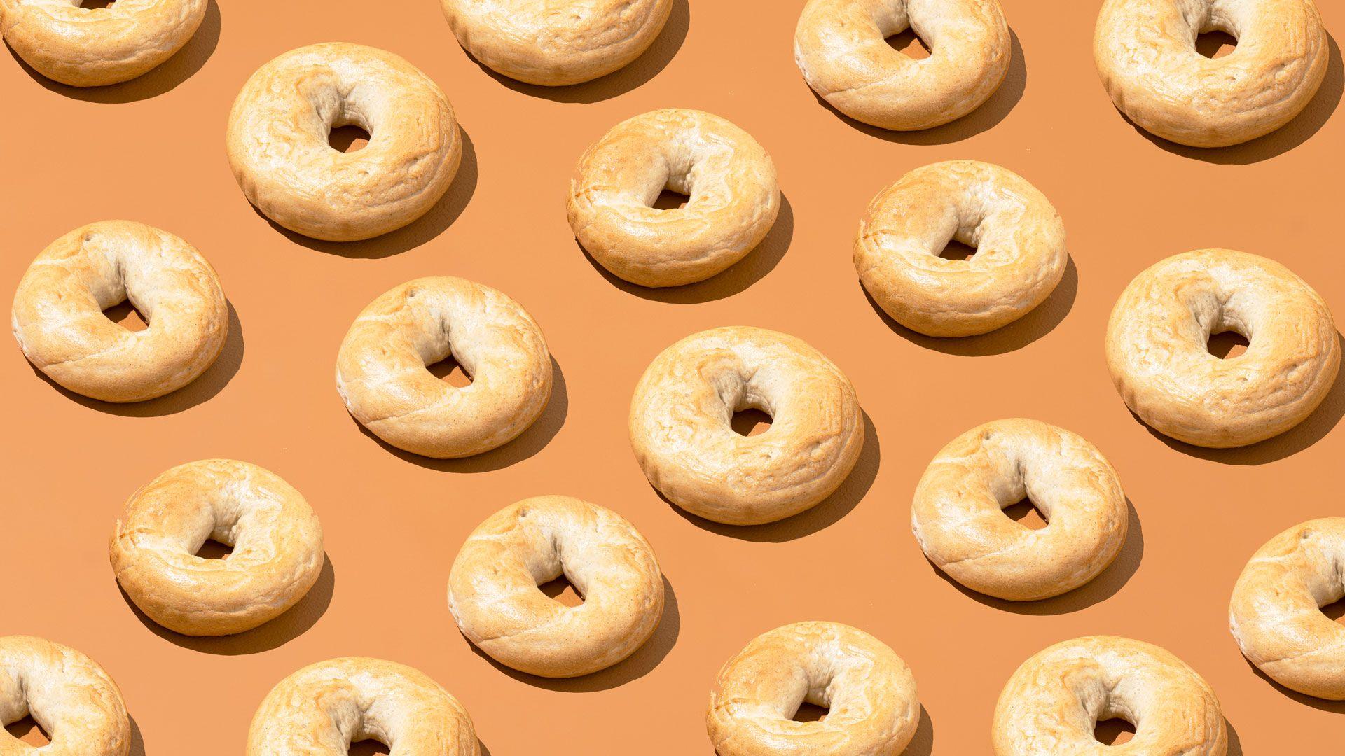 Cut out of bagels lined up in diagonal rows on a pale orange background. 