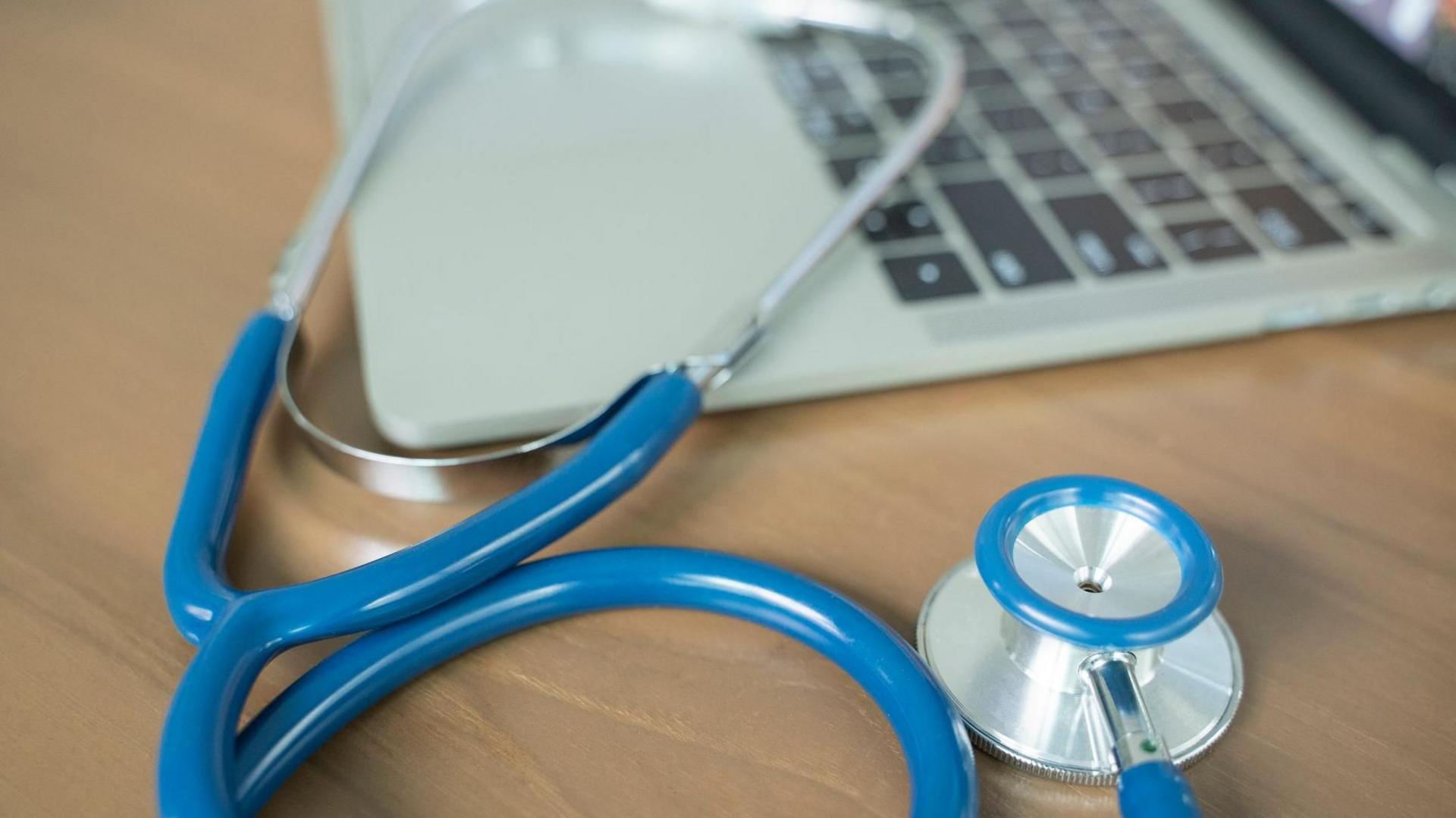 A doctor's desk with a blue stethoscope and laptop.