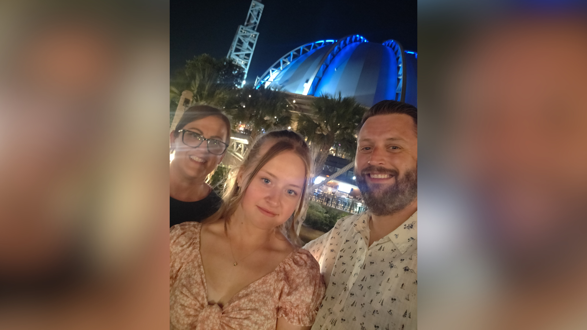 A young woman is standing in the middle of her mum and dad smiling at the camera.