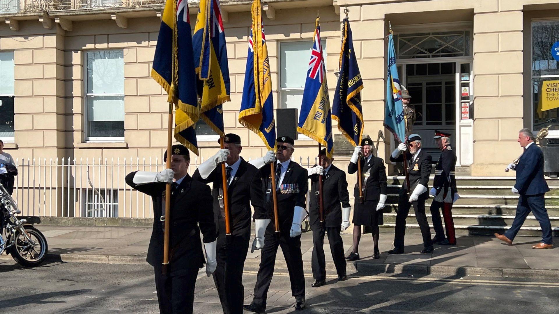 Local and international serving personnel, veterans, and local councillors pay tribute for OP TELIC. Men in uniform holding flags in a straight line.