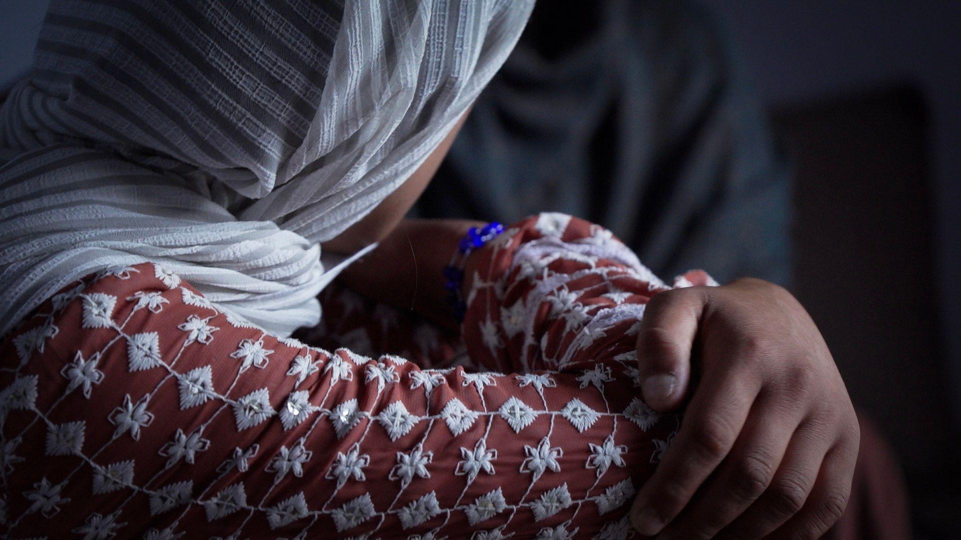 Young woman wears a white headscarf with her arms crossed over her knees.