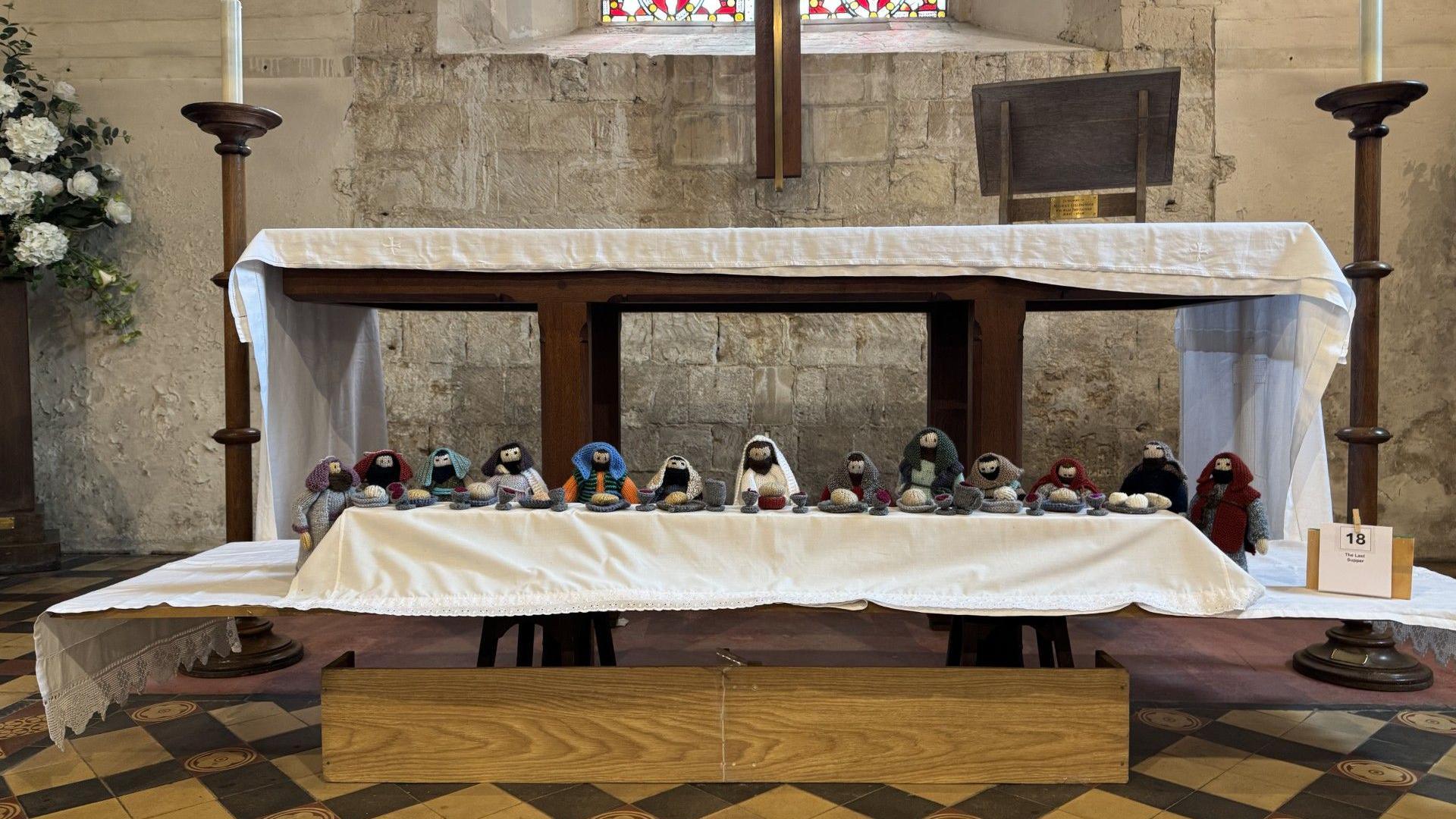 Thirteen knitted figures depicting Jesus and the Disciples at the Last Supper are laid out under the full size altar of the church.