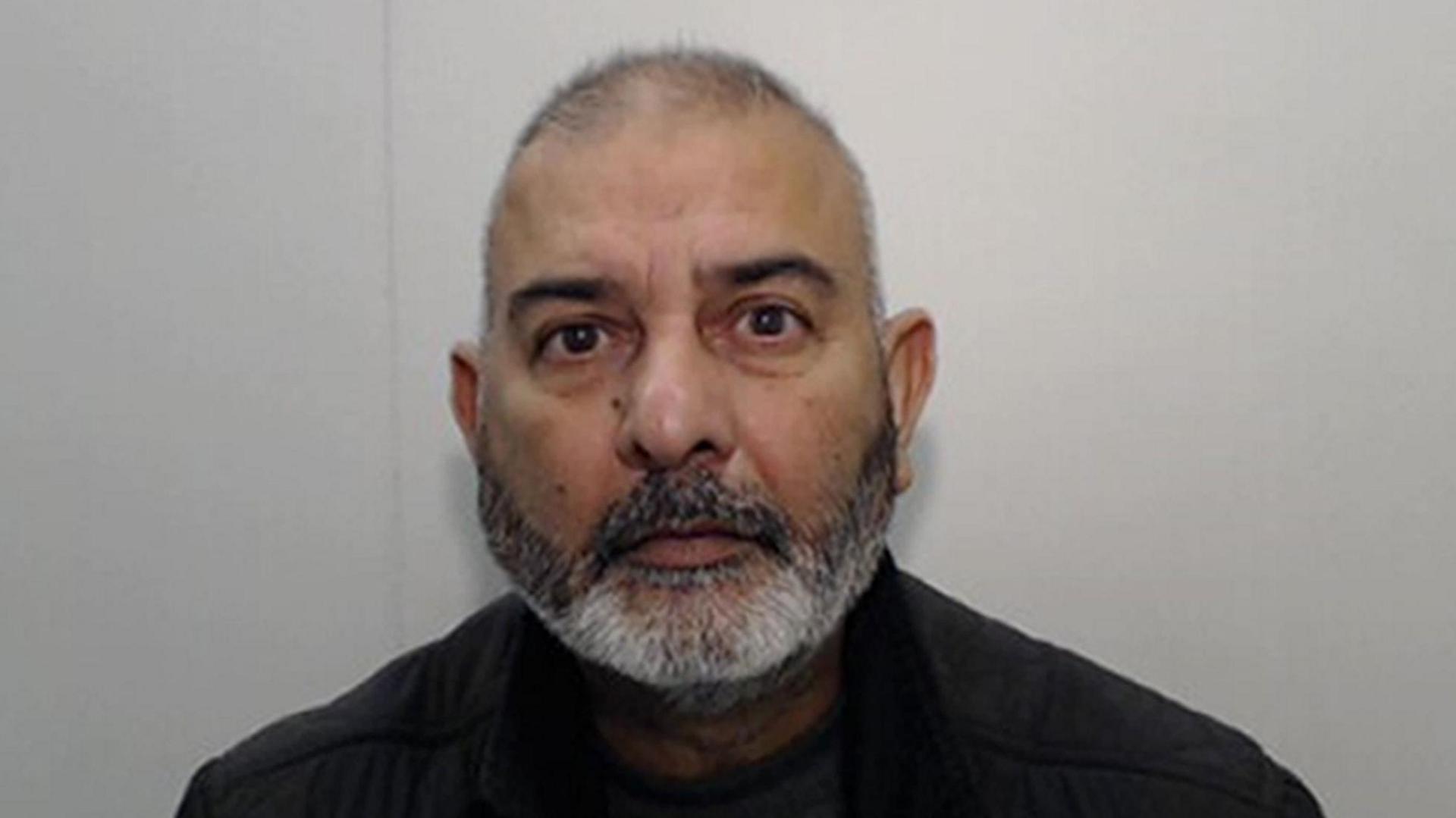 Prison headshot of Mohammed Zahid stood in front of a grey background. He is an Asian man, bald with a salt-and-pepper beard. 