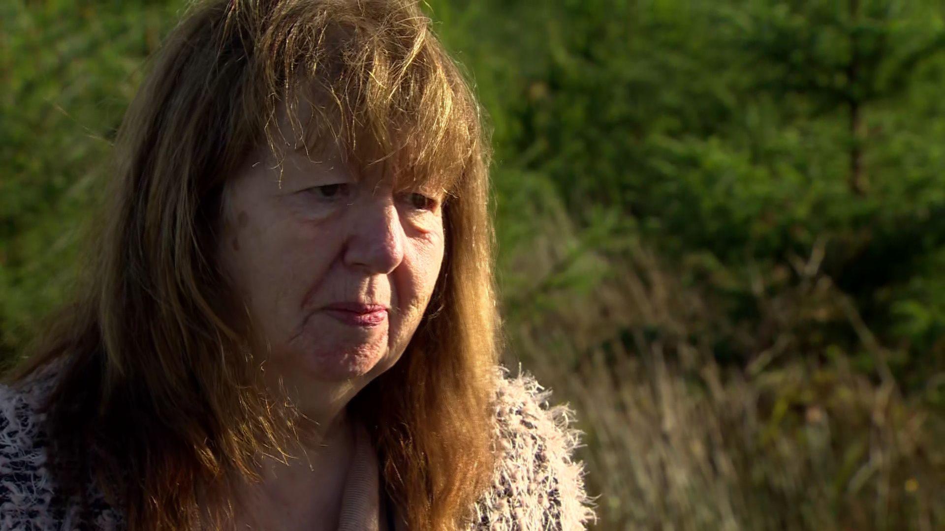 Dympna Kerr a woman with long brown hair, pictured from the neck up against a grassy bush