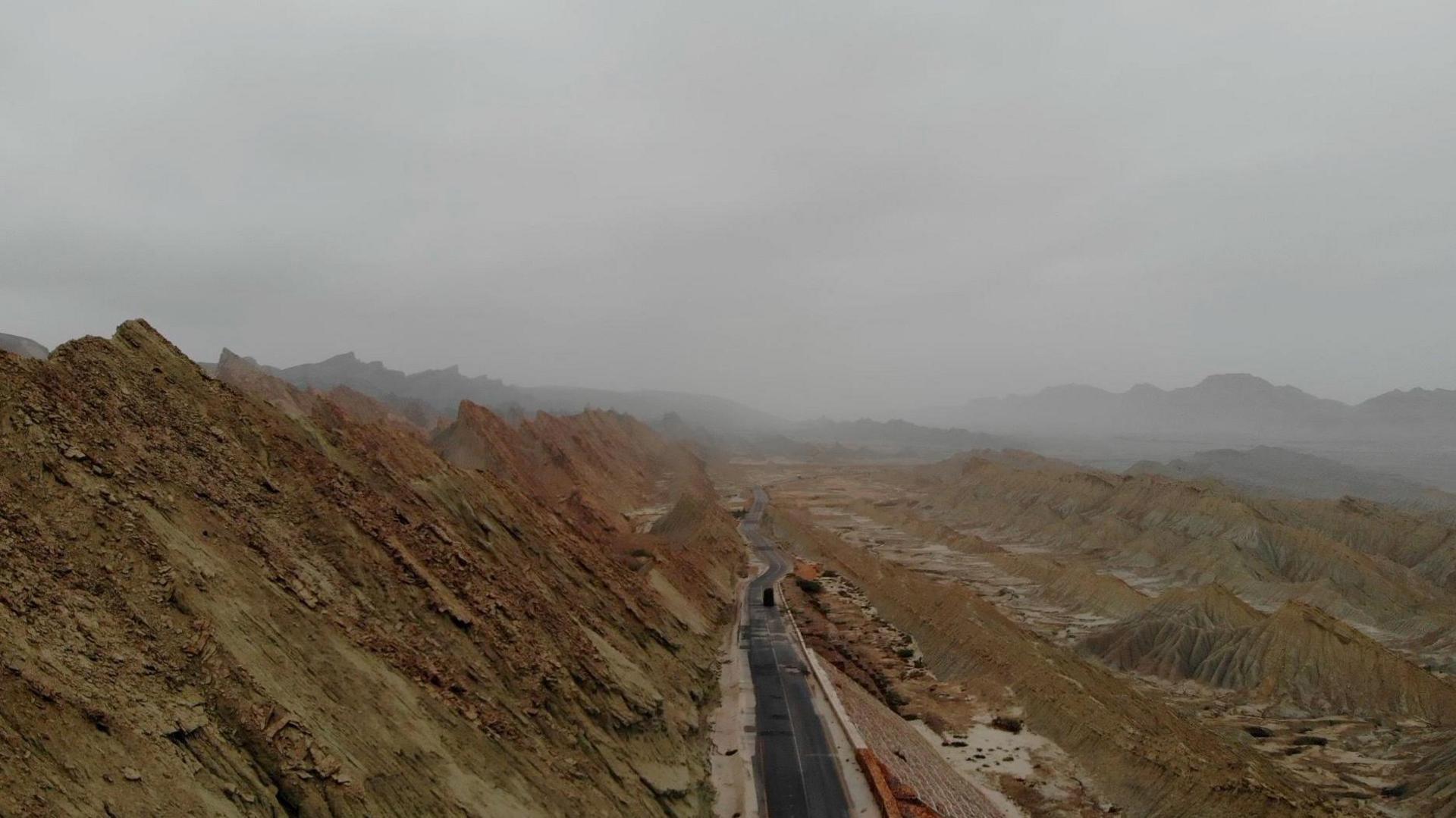 A road running between brown, barren hills in Balochistan as the landscapestretches endlessly on either side 