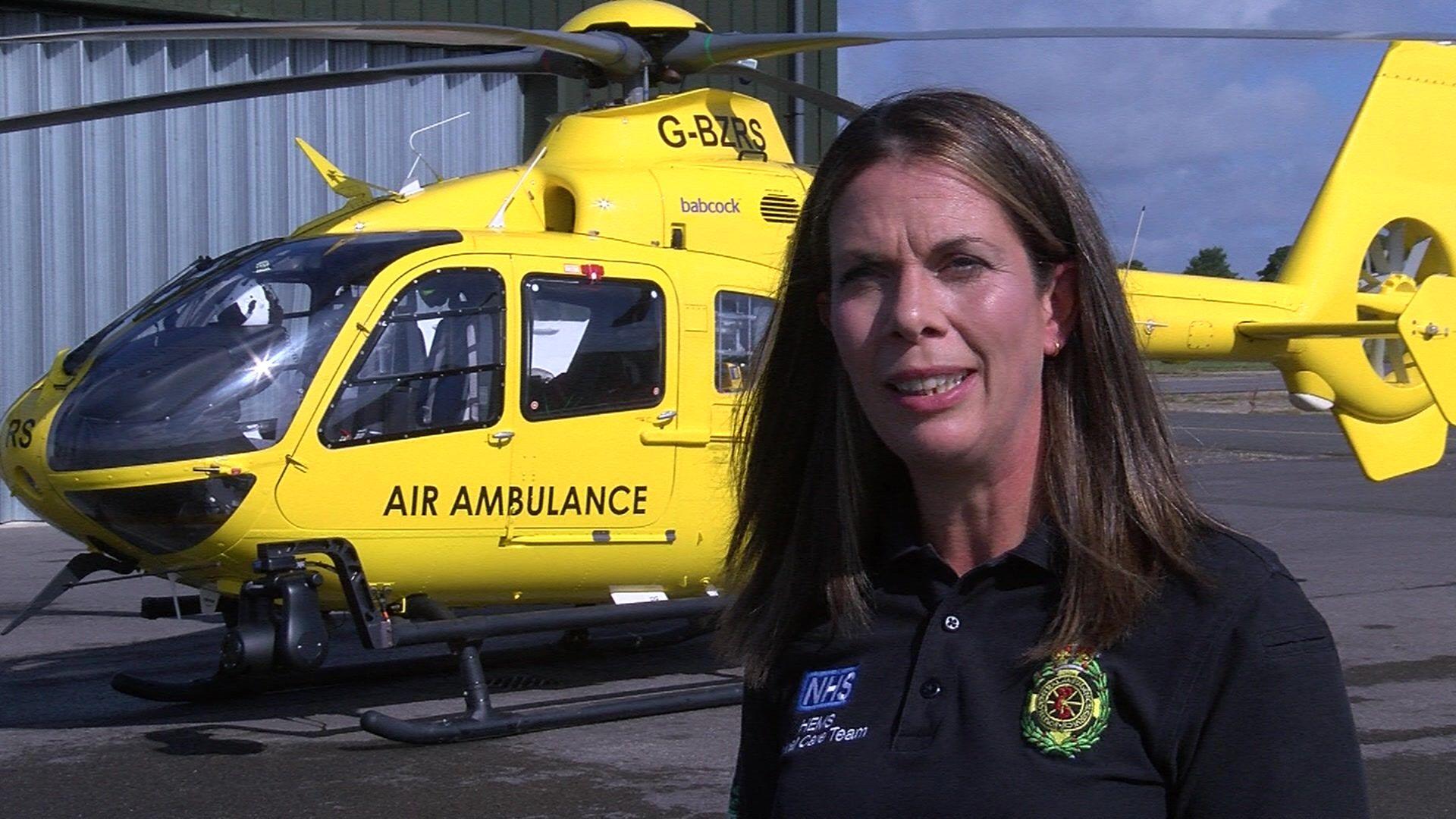 Nicola Hawkes from the shoulders up, in the background there is a bright yellow helicopter.