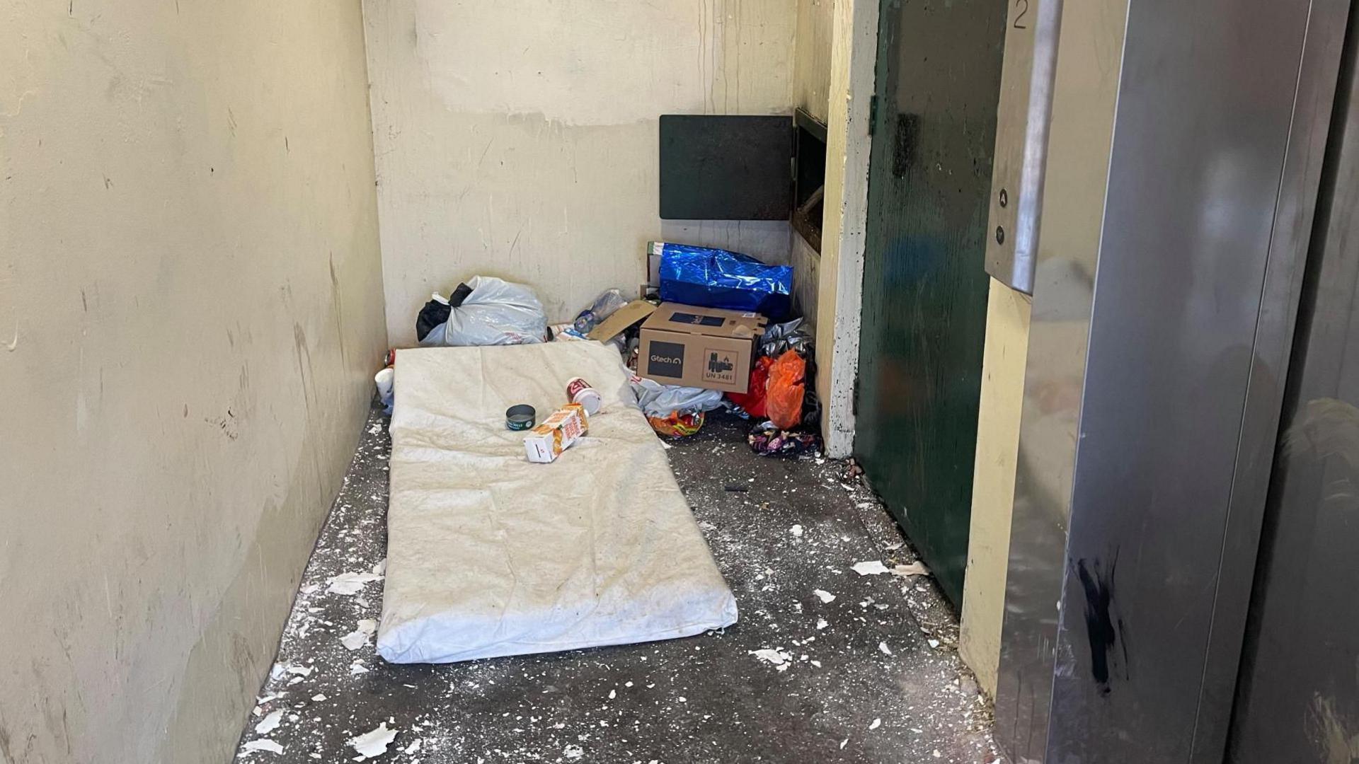 A mattress and other discarded rubbish piled up outside lifts.