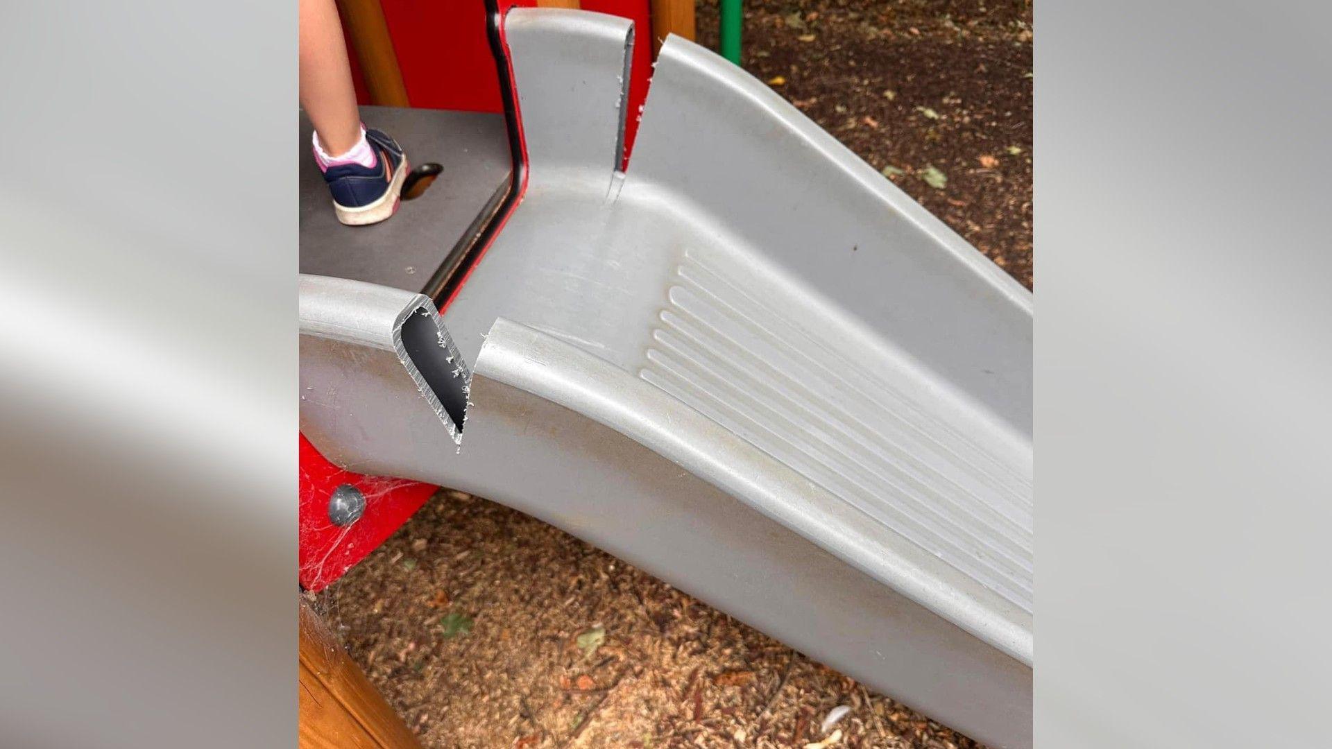 A grey children's slide with chainsaw damage