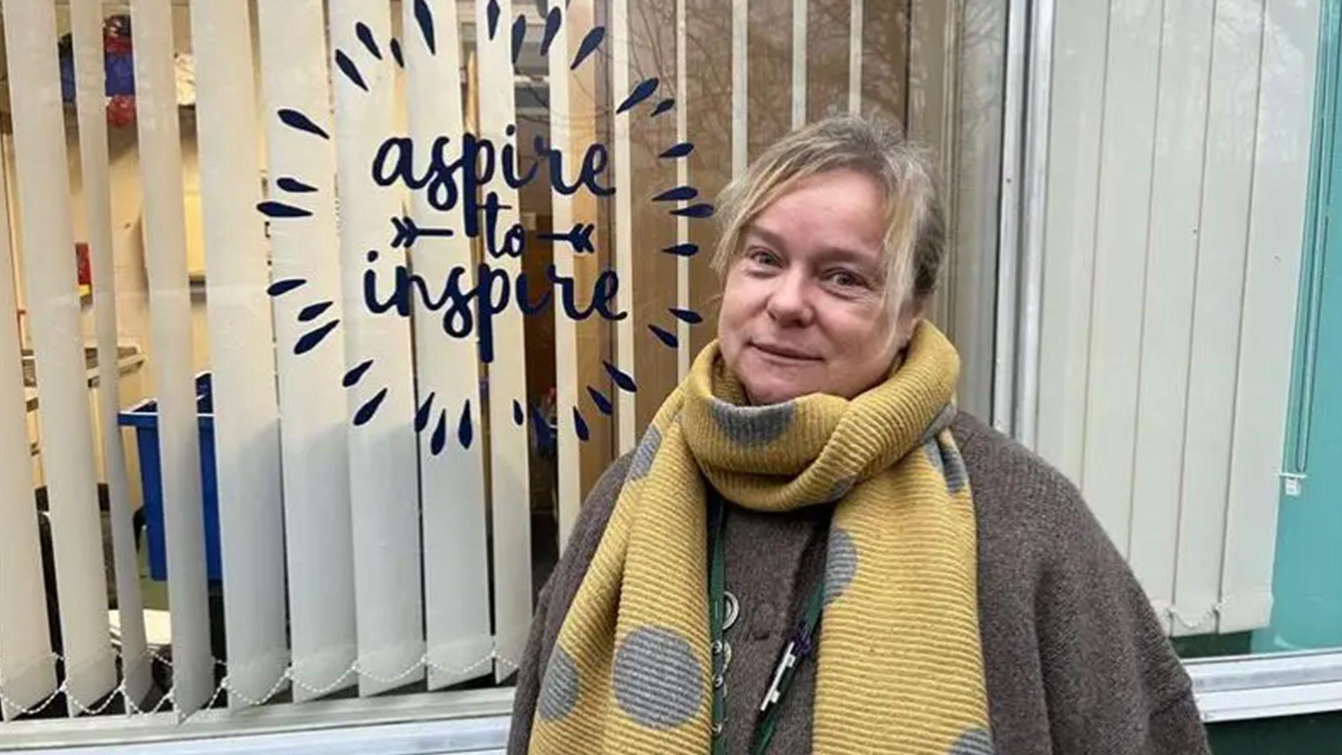 A headteacher standing next to a window mural that says "aspire to inspire".